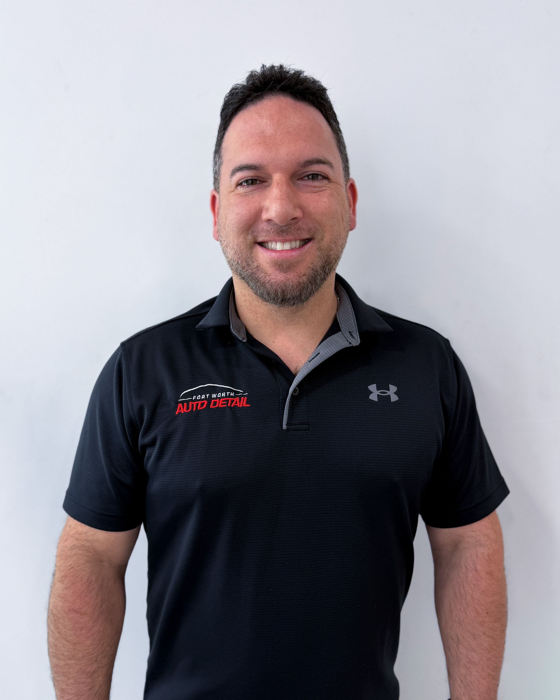 Smiling person in a black polo shirt standing against a light wall