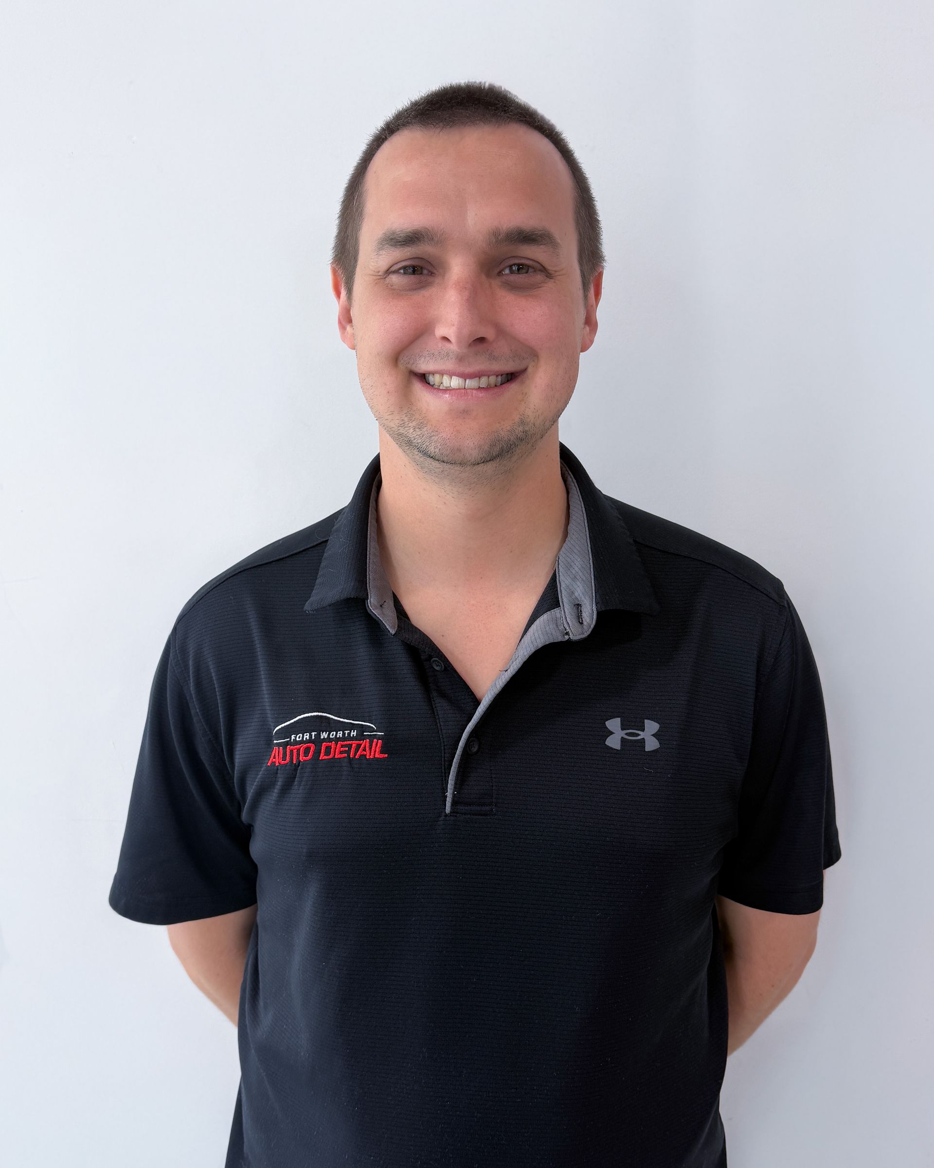 Smiling person in a dark navy polo shirt standing against a light wall.