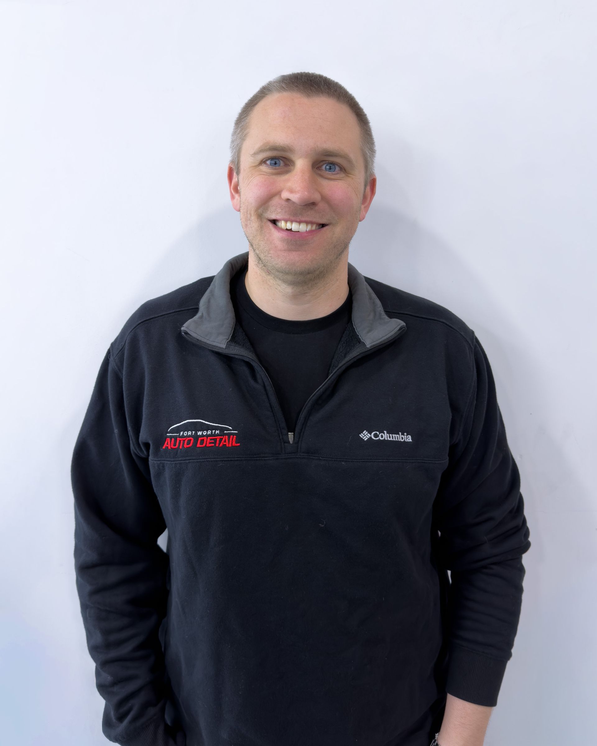 Smiling person in a dark jacket standing against a white background