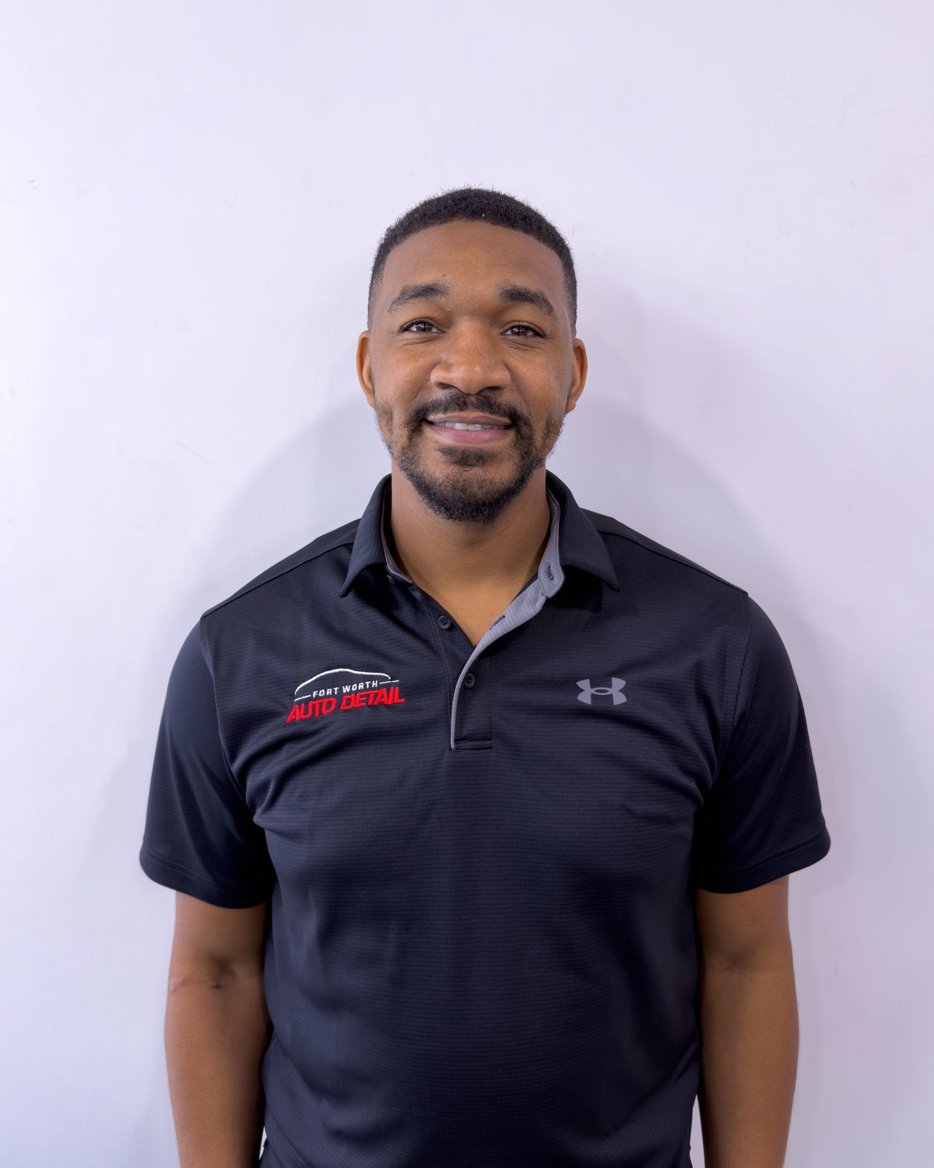 Smiling man in a black polo shirt standing against a plain light background