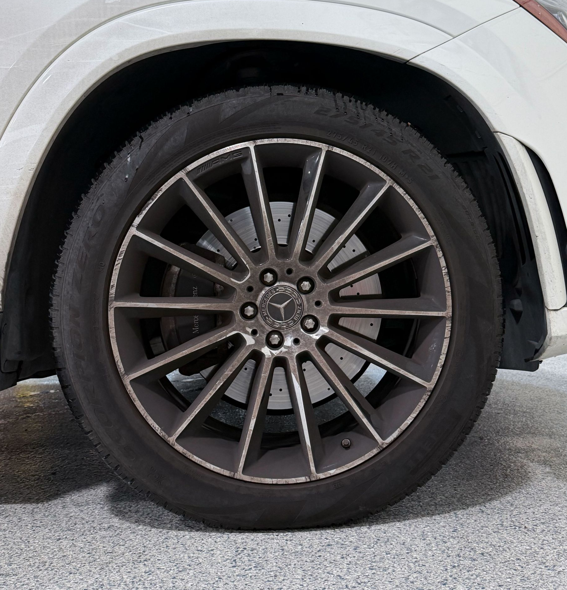 Close-up of a car wheel with a dark alloy rim and black tire on a white vehicle.