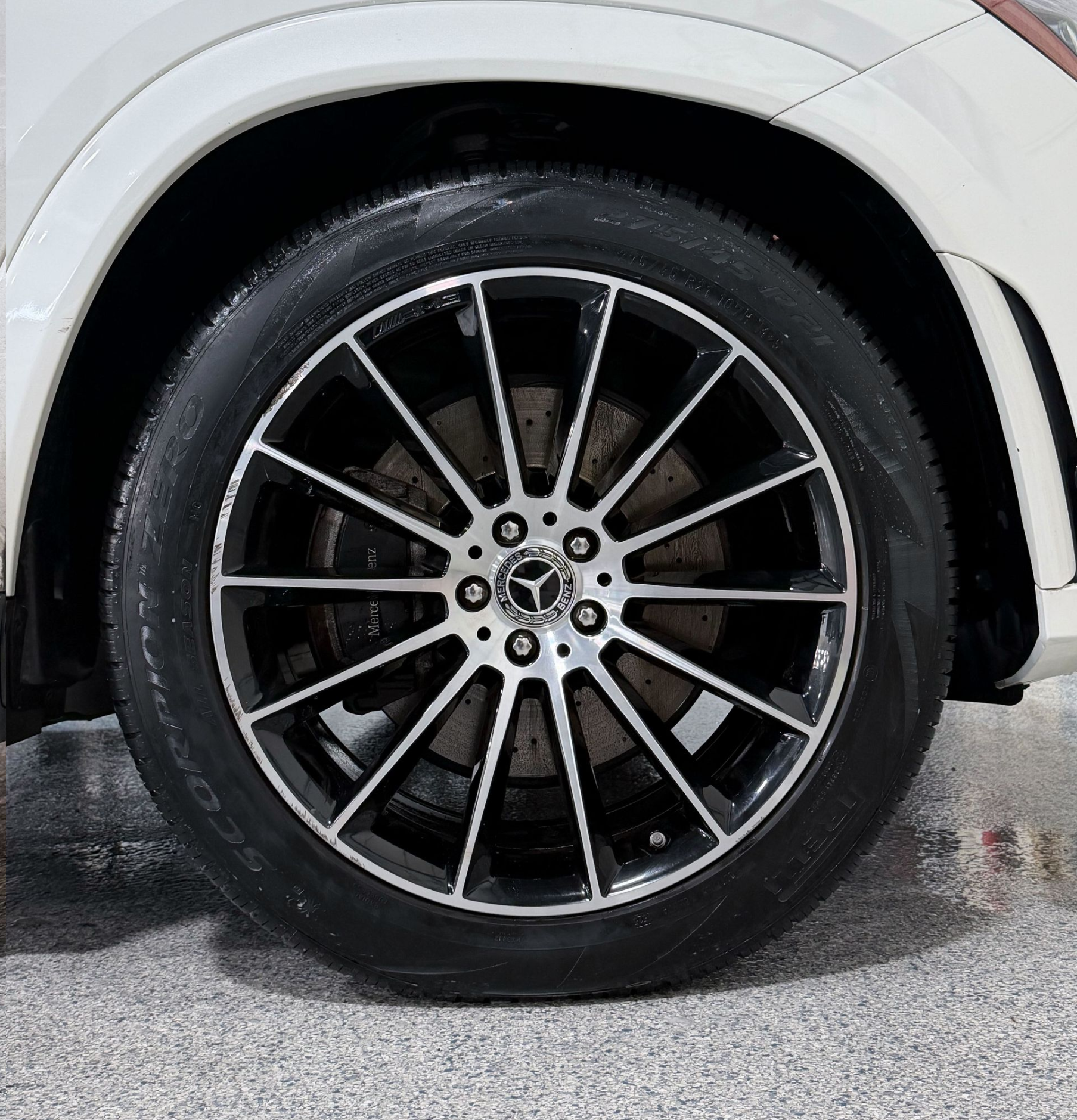 Close-up of a white car’s front wheel with black alloy rim on a wet surface
