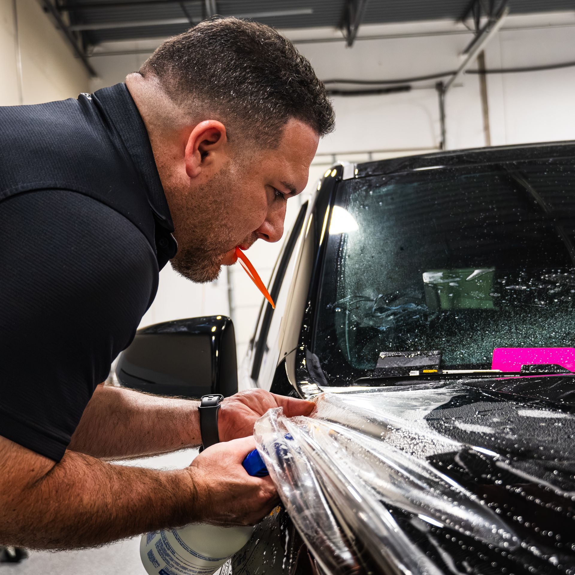 A man is spraying a car with a spray bottle and a straw.