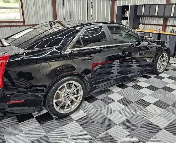 A black car is parked in a garage on a checkered floor.