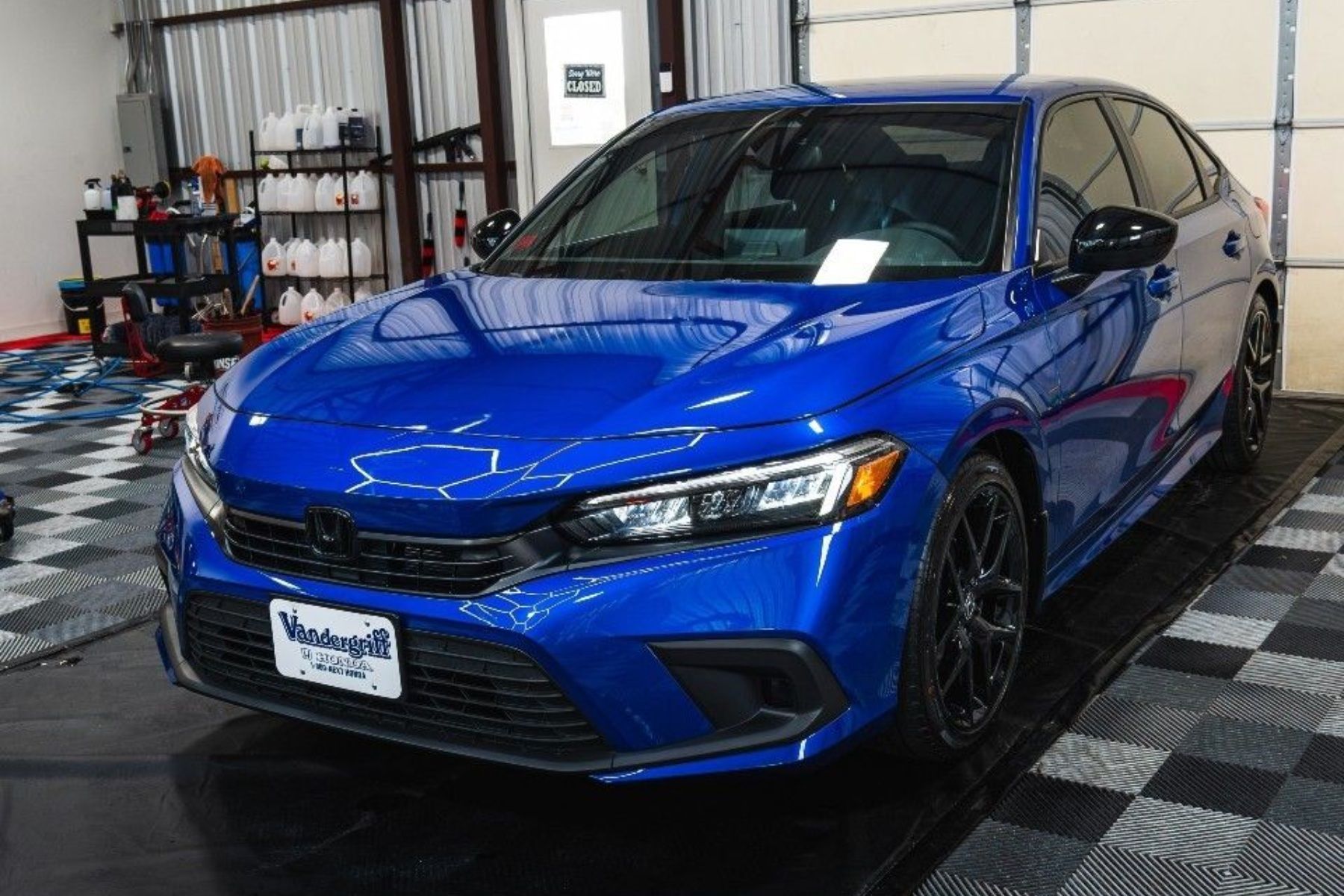 Blue sedan parked indoors in a workshop, viewed from the front-left side.