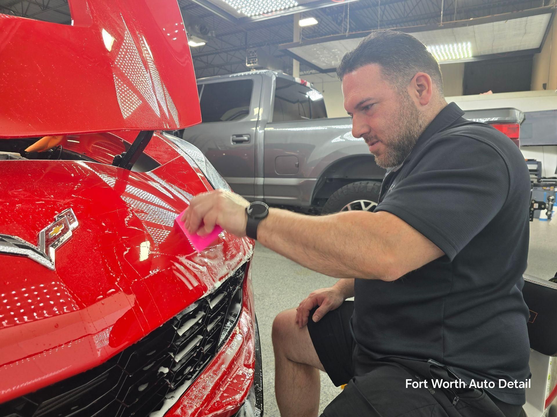 Man polishing the front of a red sports car in a dealership showroom