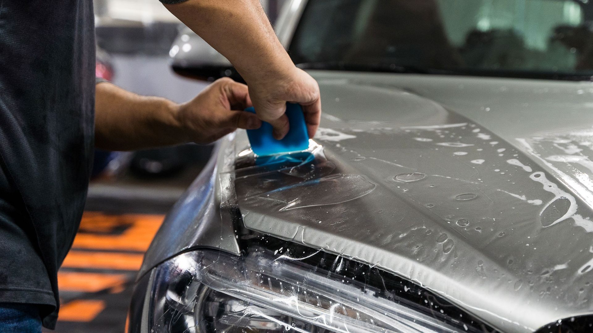 A man is applying a protective film to the hood of a car.