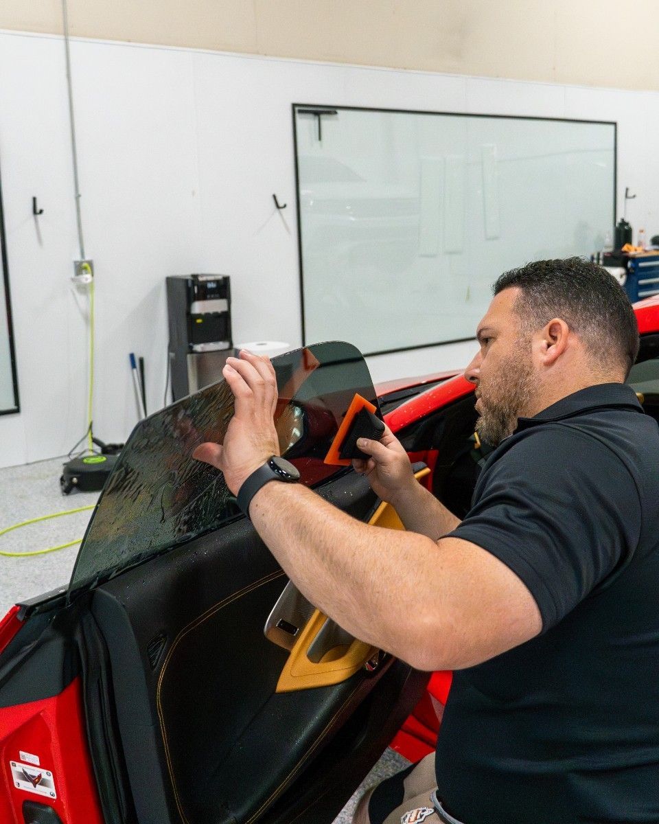 A man is installing a window tint on a red car.