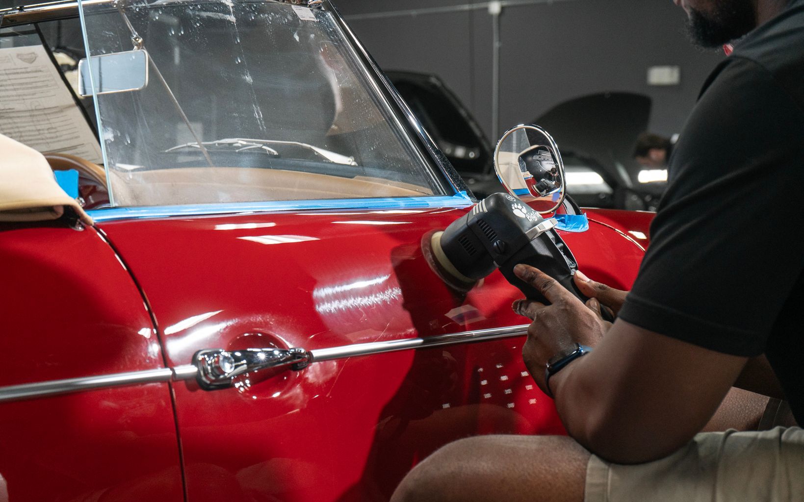 A man is polishing a red car with a machine.