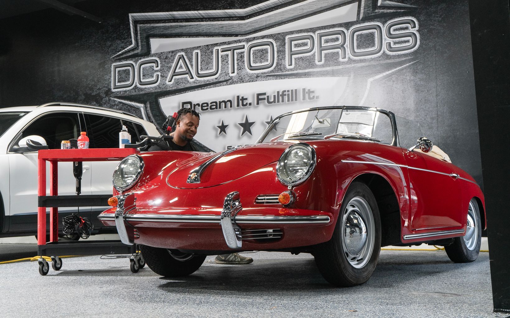 A man is working on a red car in front of a sign that says dc auto pros