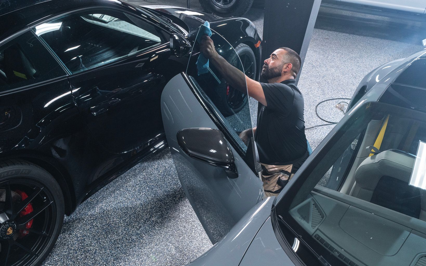 A man is cleaning the windows of a car in a garage.