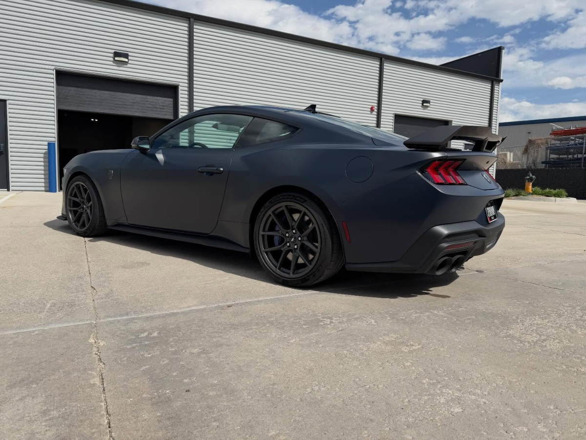 Matte black Ford Mustang GT with rear spoiler and dark alloy wheels parked outside automotive shop