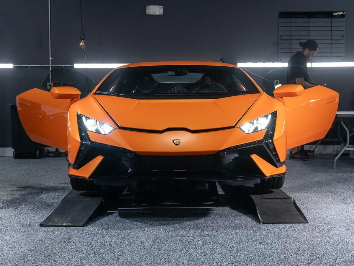 Orange Lamborghini sports car with both doors open inside a detailing studio.