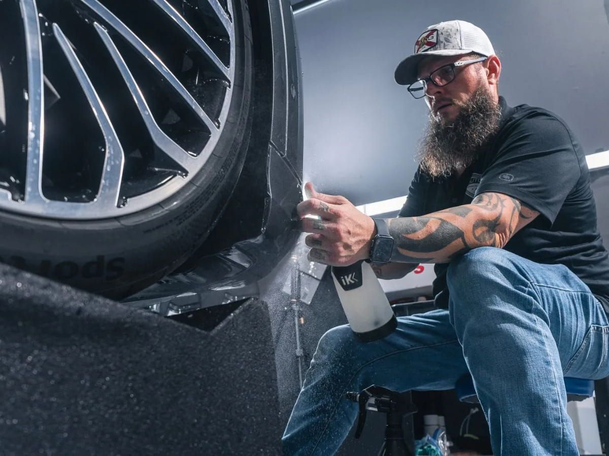 Detailer cleaning the wheel arch of a dark vehicle with a spray bottle.