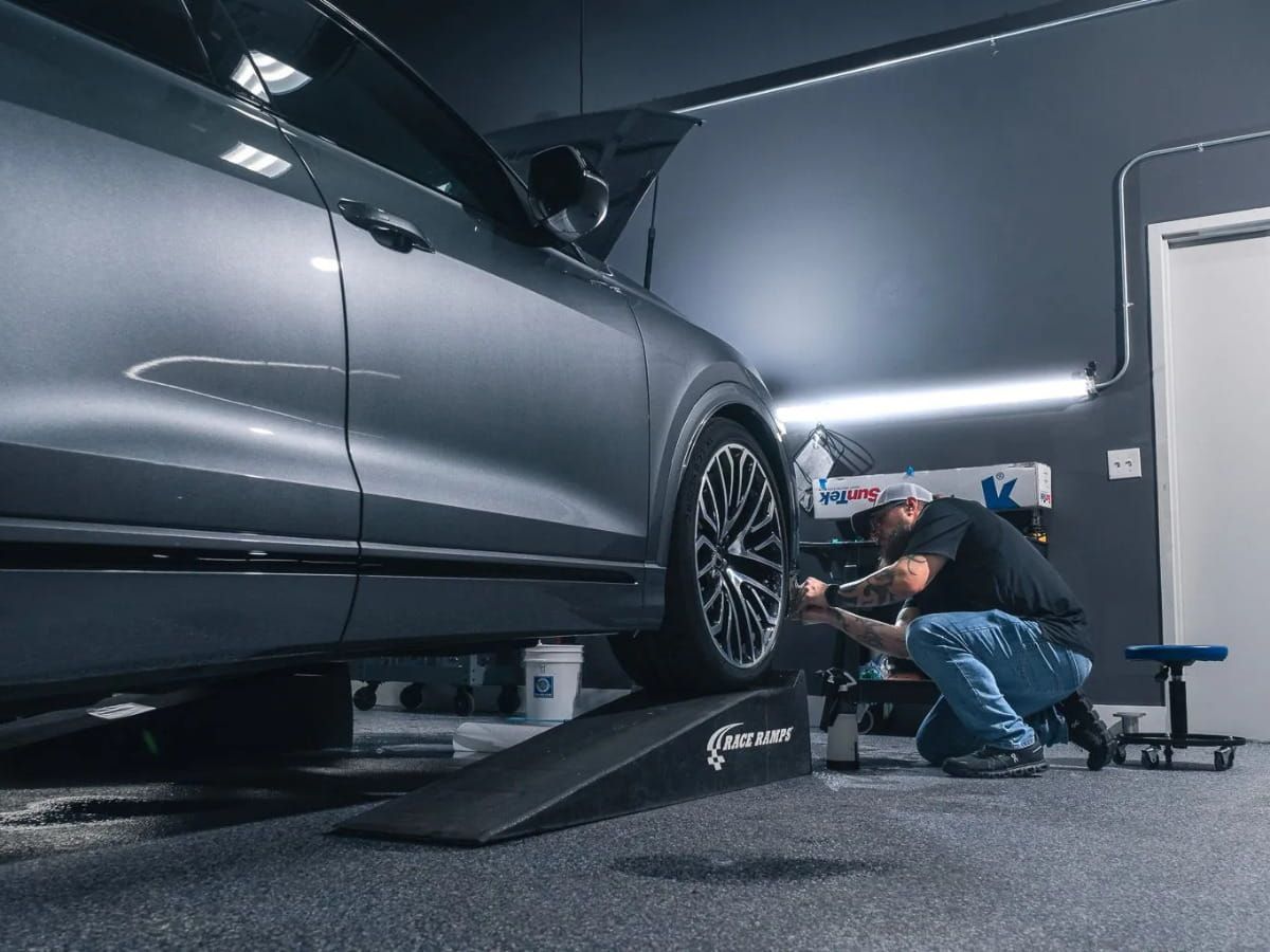 Detailer inspecting or cleaning the underside of a vehicle with a blue applicator.