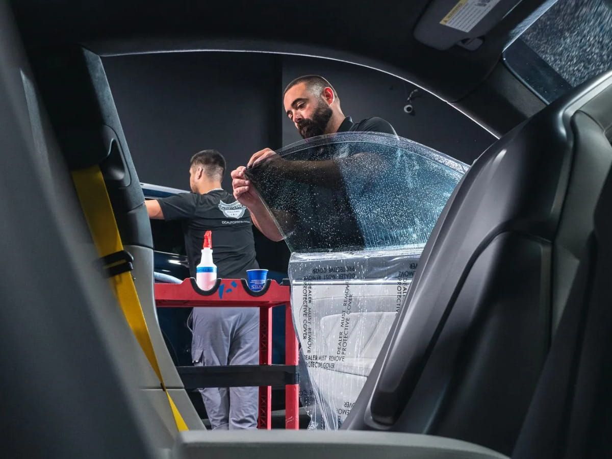 Technician applying window tint film to a vehicle side window.