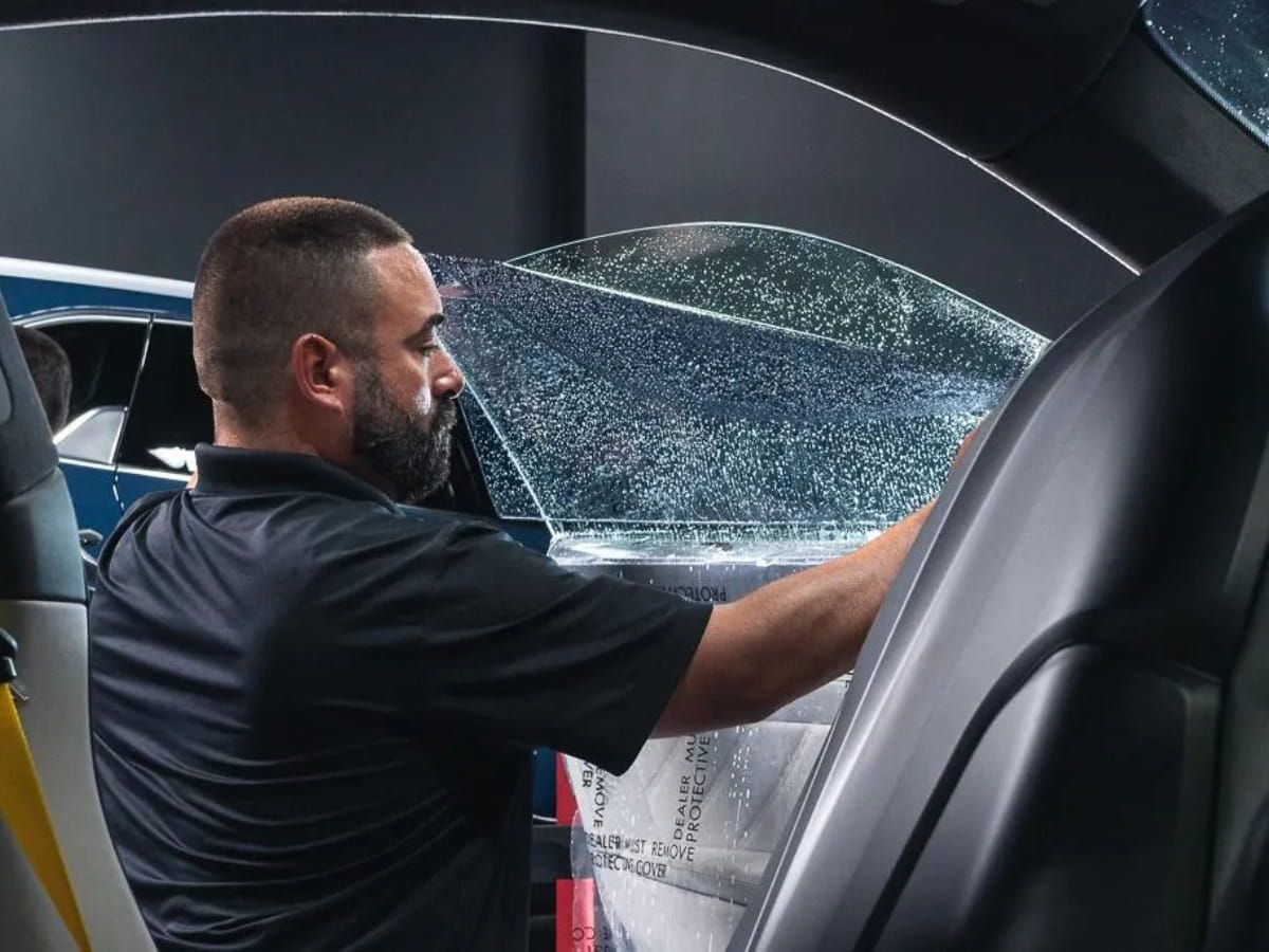 Technician installing window tint on a vehicle side window.