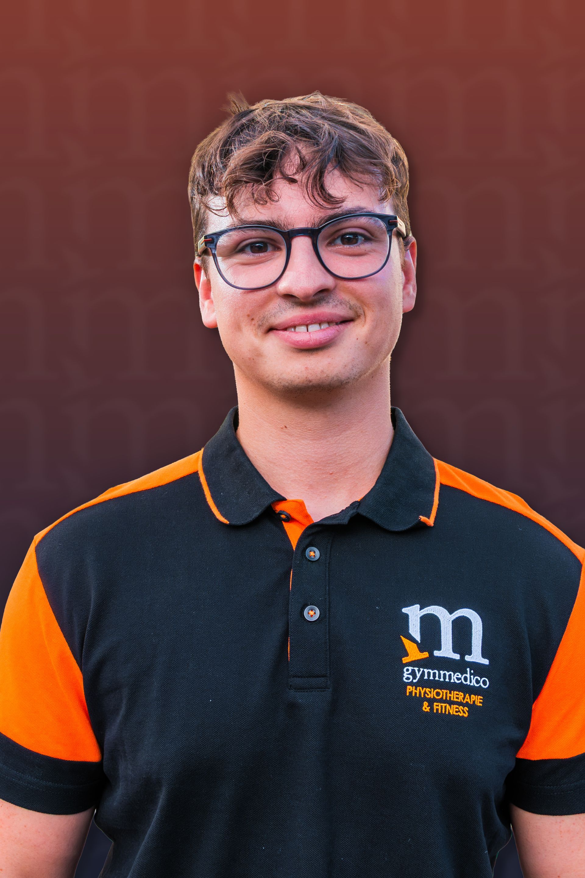 Lächelnde Person mit Brille und schwarz-orangem Poloshirt vor bordeauxrotem Hintergrund