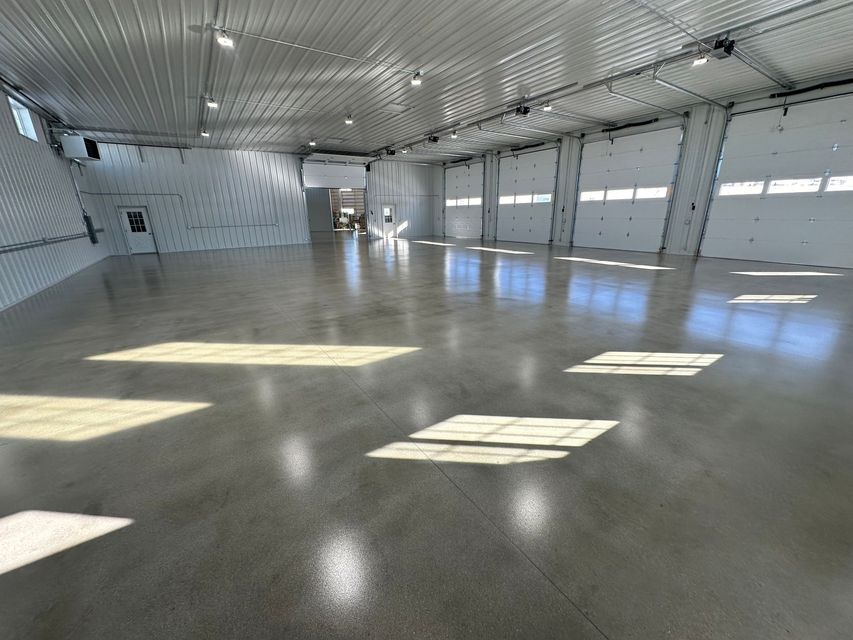 Empty bright warehouse interior with polished concrete floor and large garage doors along the right wall