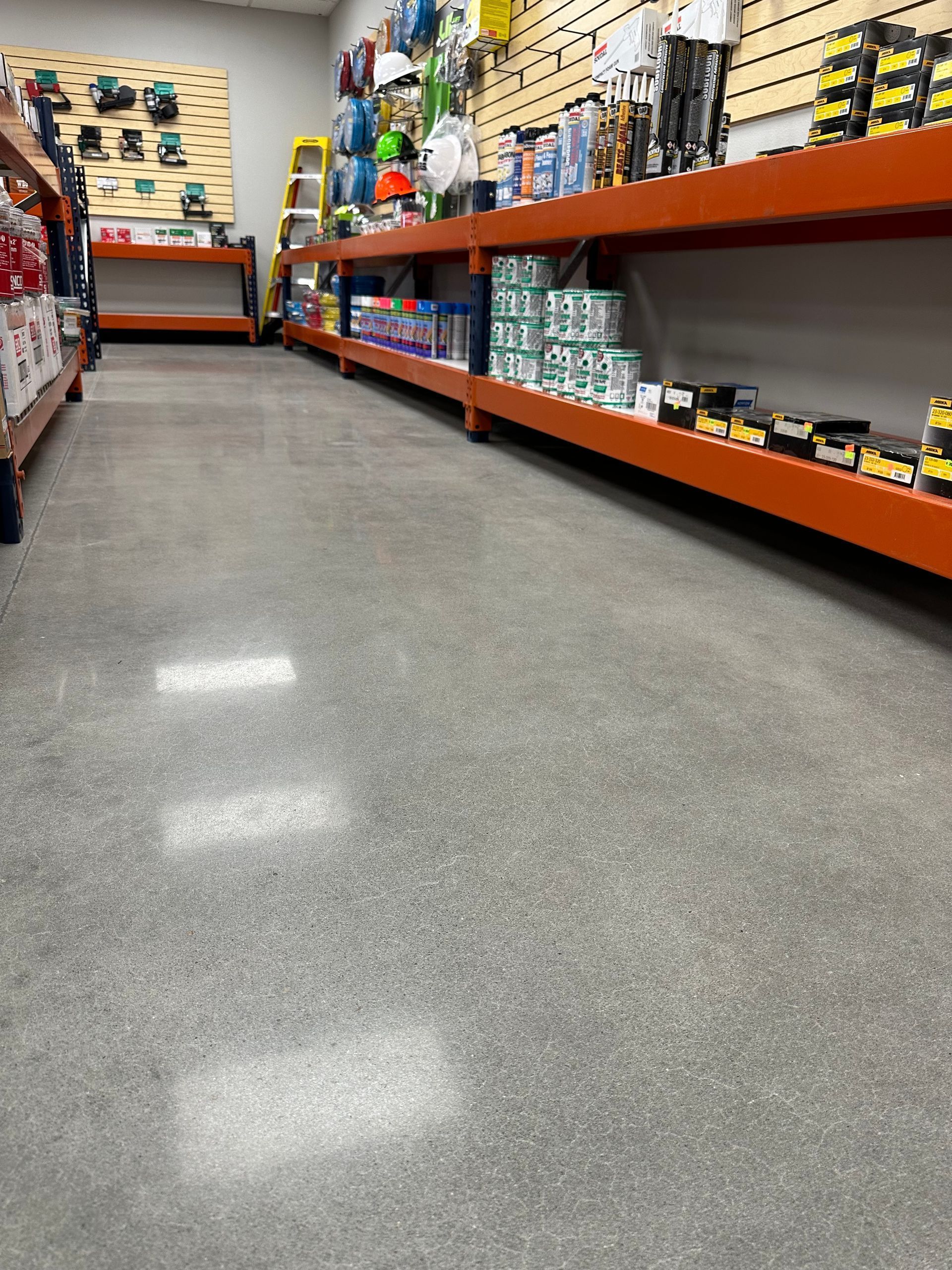 A hardware store aisle with orange shelves stocked with tools and supplies.