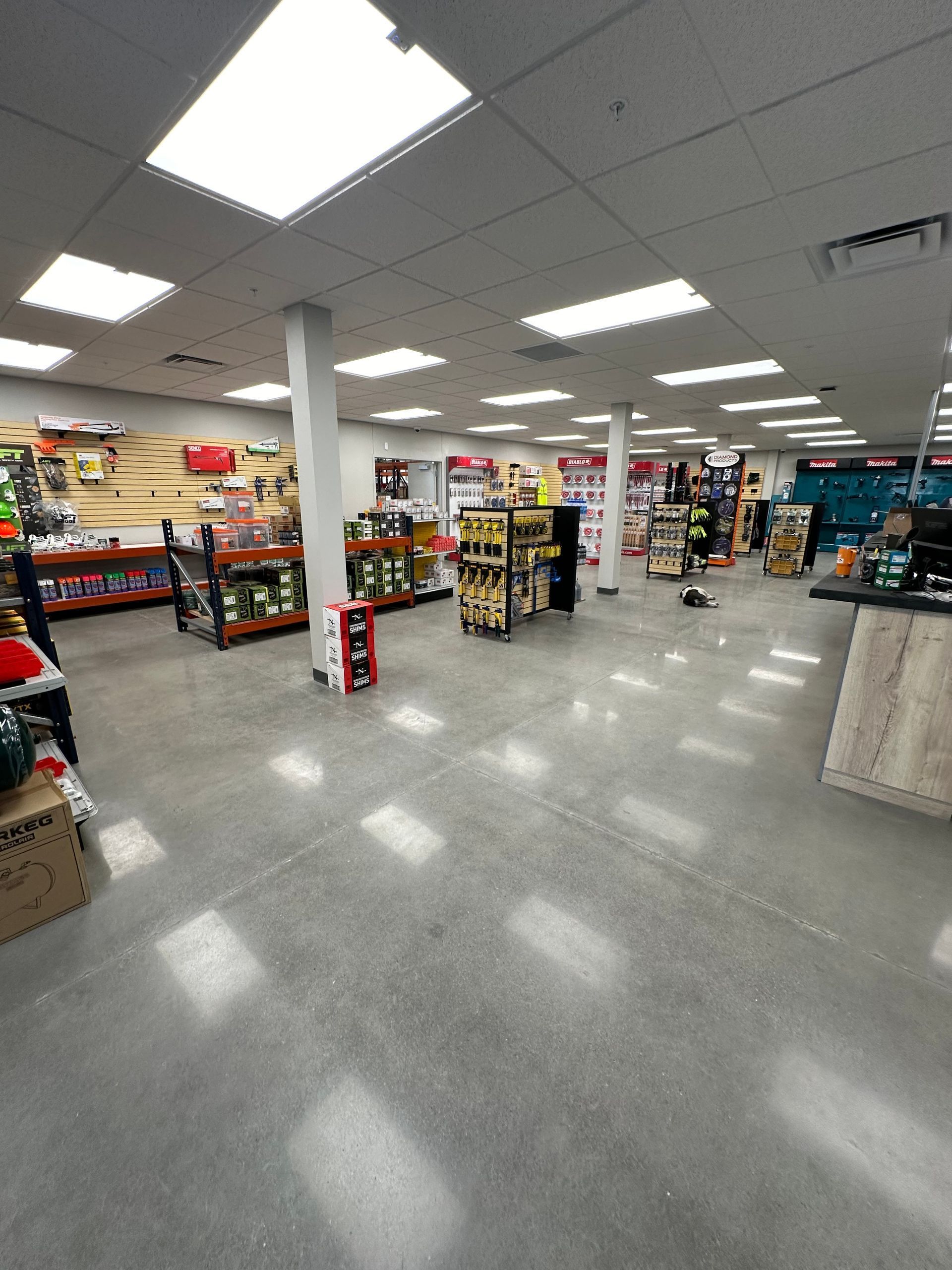 Wide view of a brightly lit convenience store aisle with shelves, displays, and gray tile floors