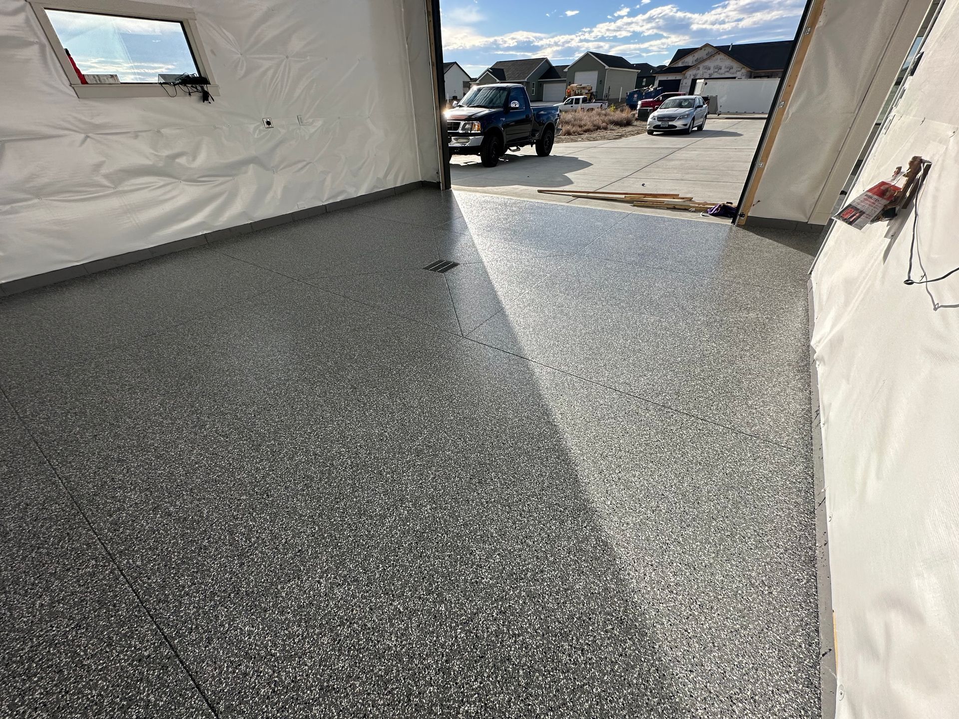 Speckled gray flooring inside a white tent, looking out to a driveway with parked vehicles.