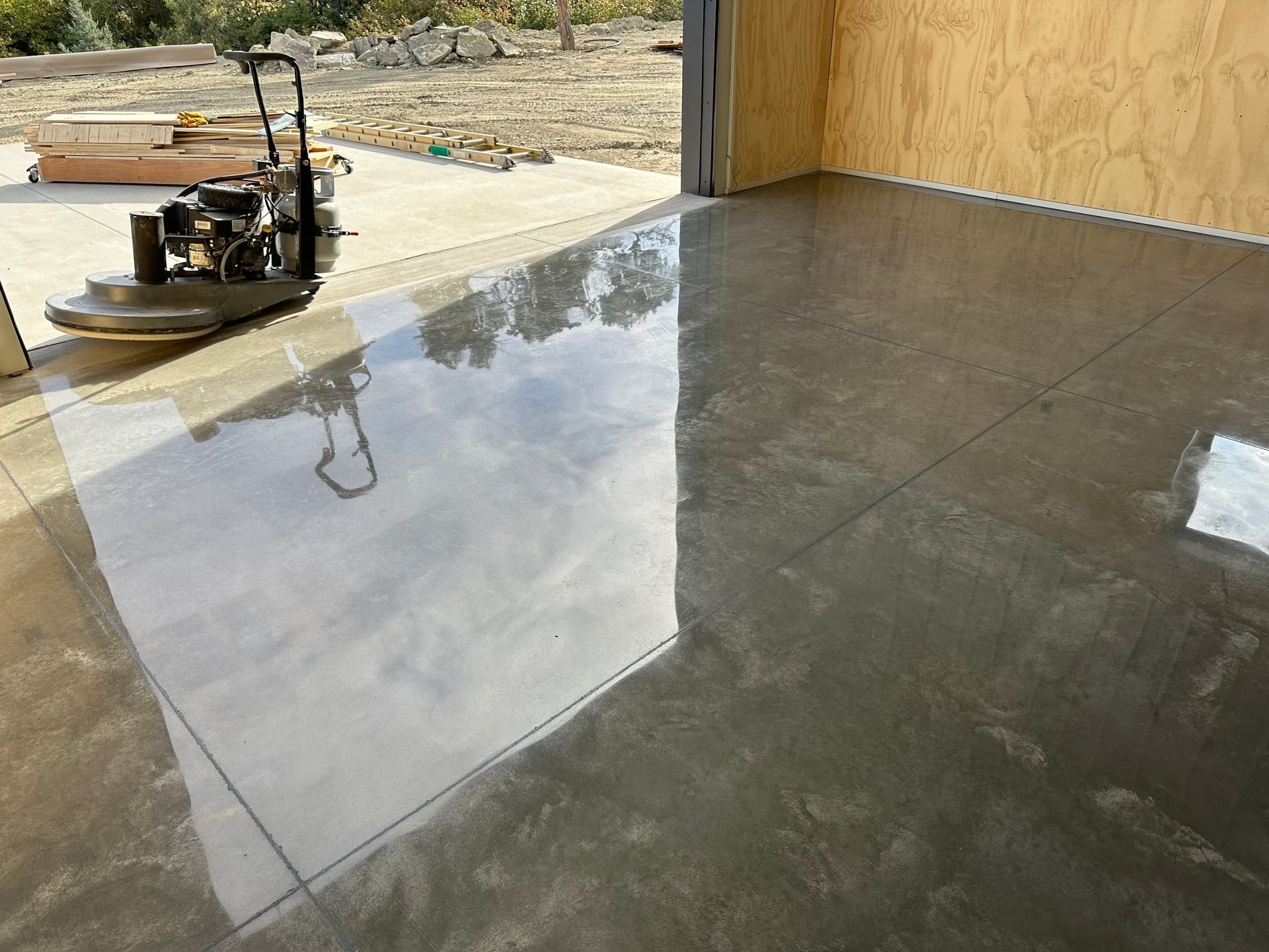 Wet concrete floor inside a building under construction, reflecting light from a large opening.