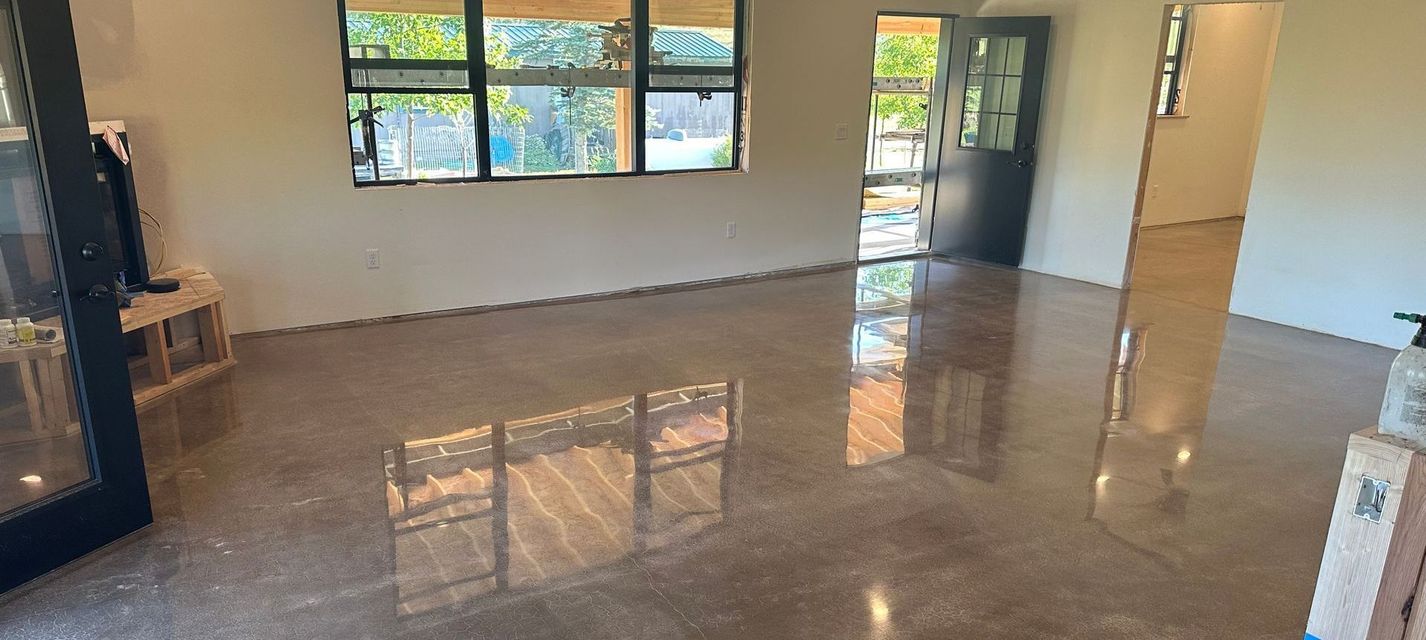Empty polished living room with large windows, open doorway, and sunlight reflecting on the floor
