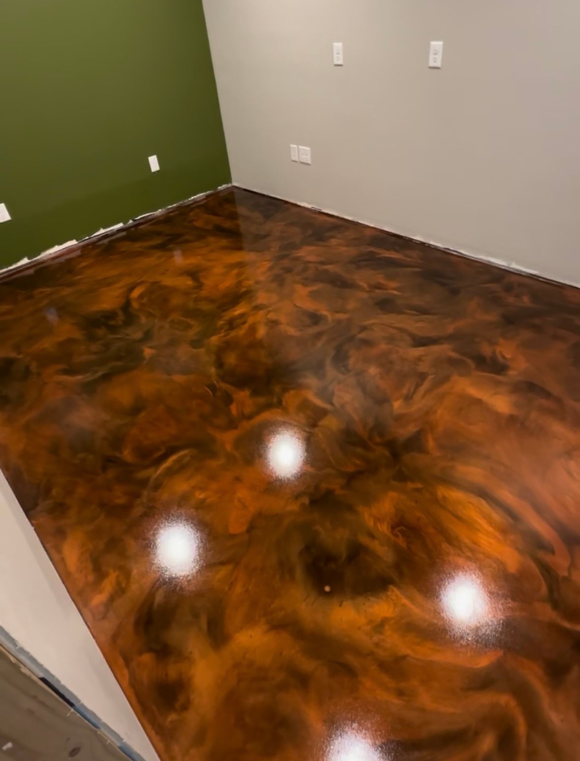 Empty room with glossy brown marbled floor, green and white walls, and electrical outlets.