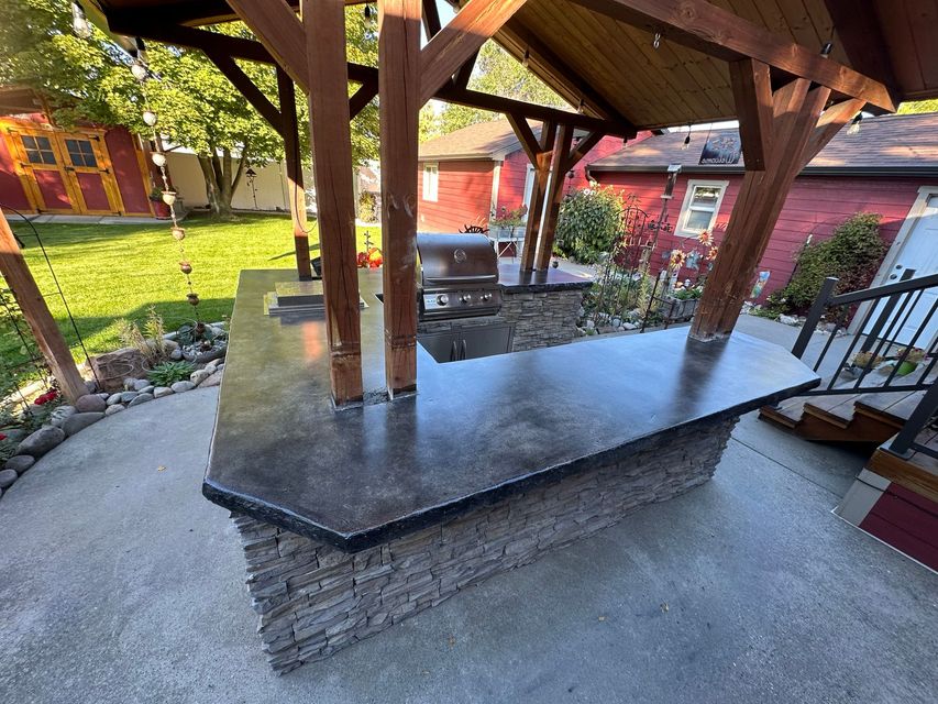 Covered outdoor patio with a black stone counter and wooden support posts in a garden yard
