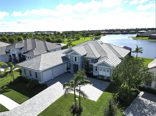 Aerial view of a light blue house with a gray tile roof and driveway; a lake and other houses are in the background.