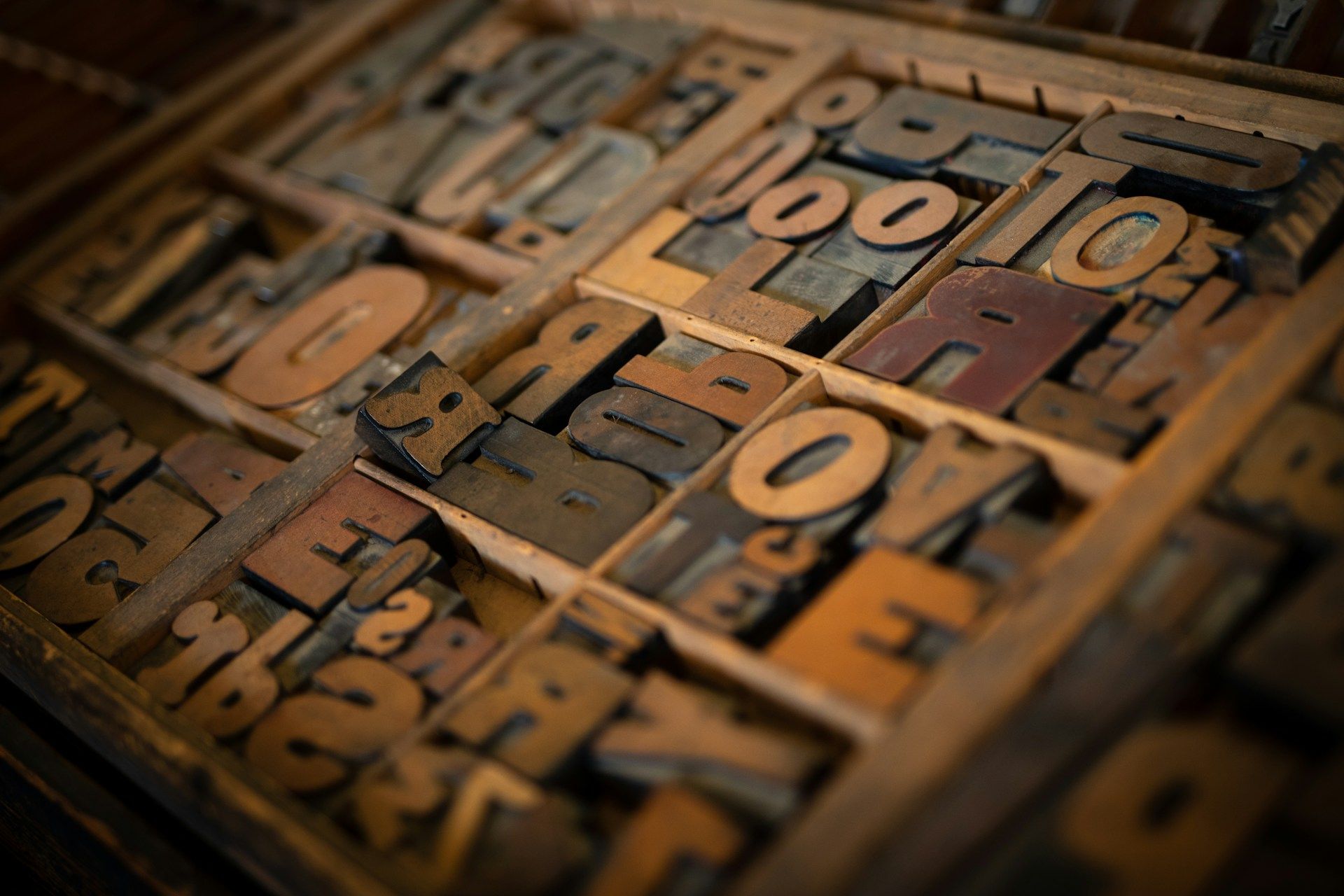 Wooden type blocks in a compartmentalized drawer, varying in shape and color, likely for letterpress printing.