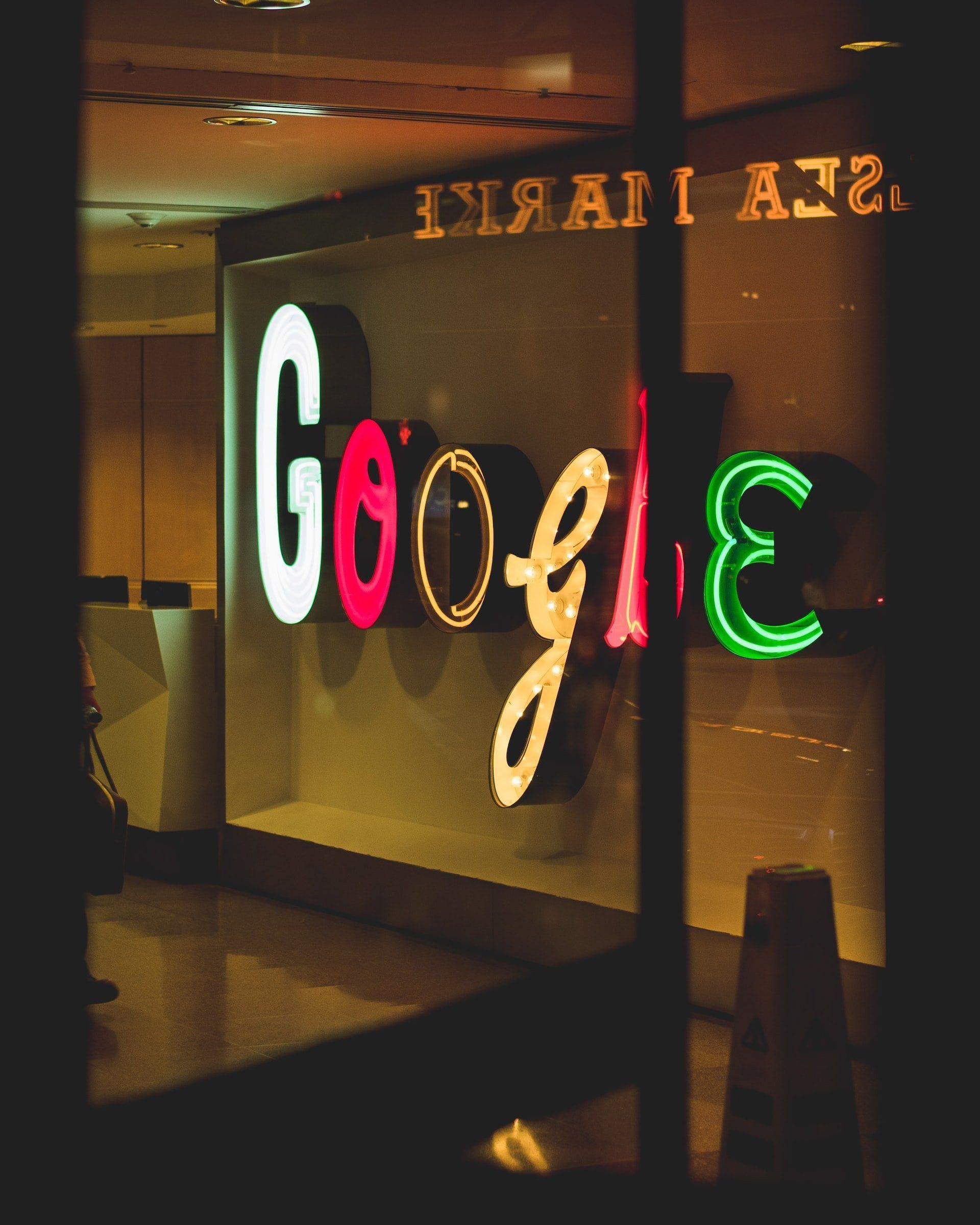 Neon Google sign in a window, with colorful illuminated letters, viewed from outside at night.