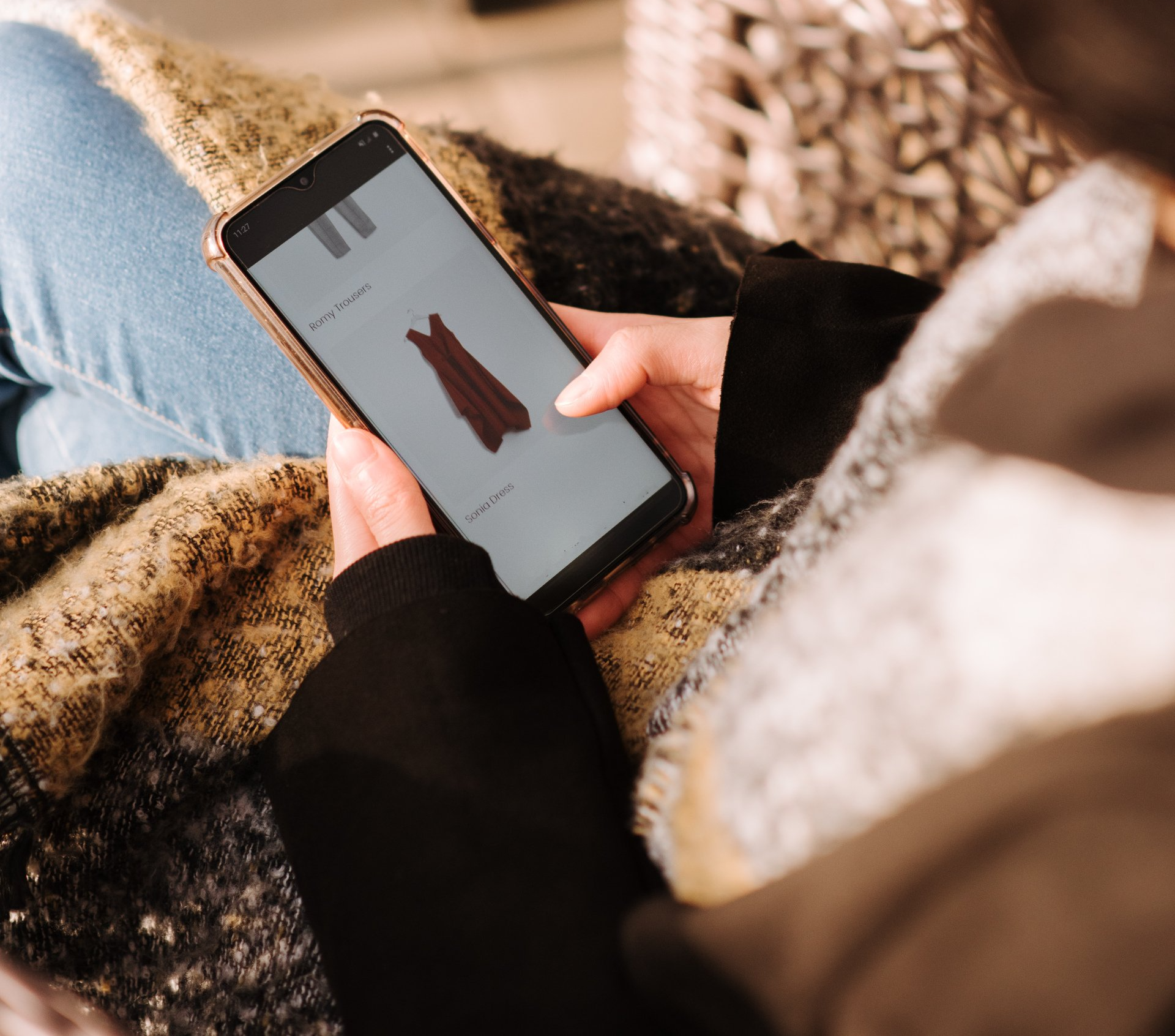 Person holding a smartphone displaying a maroon dress. They are sitting, likely shopping online.