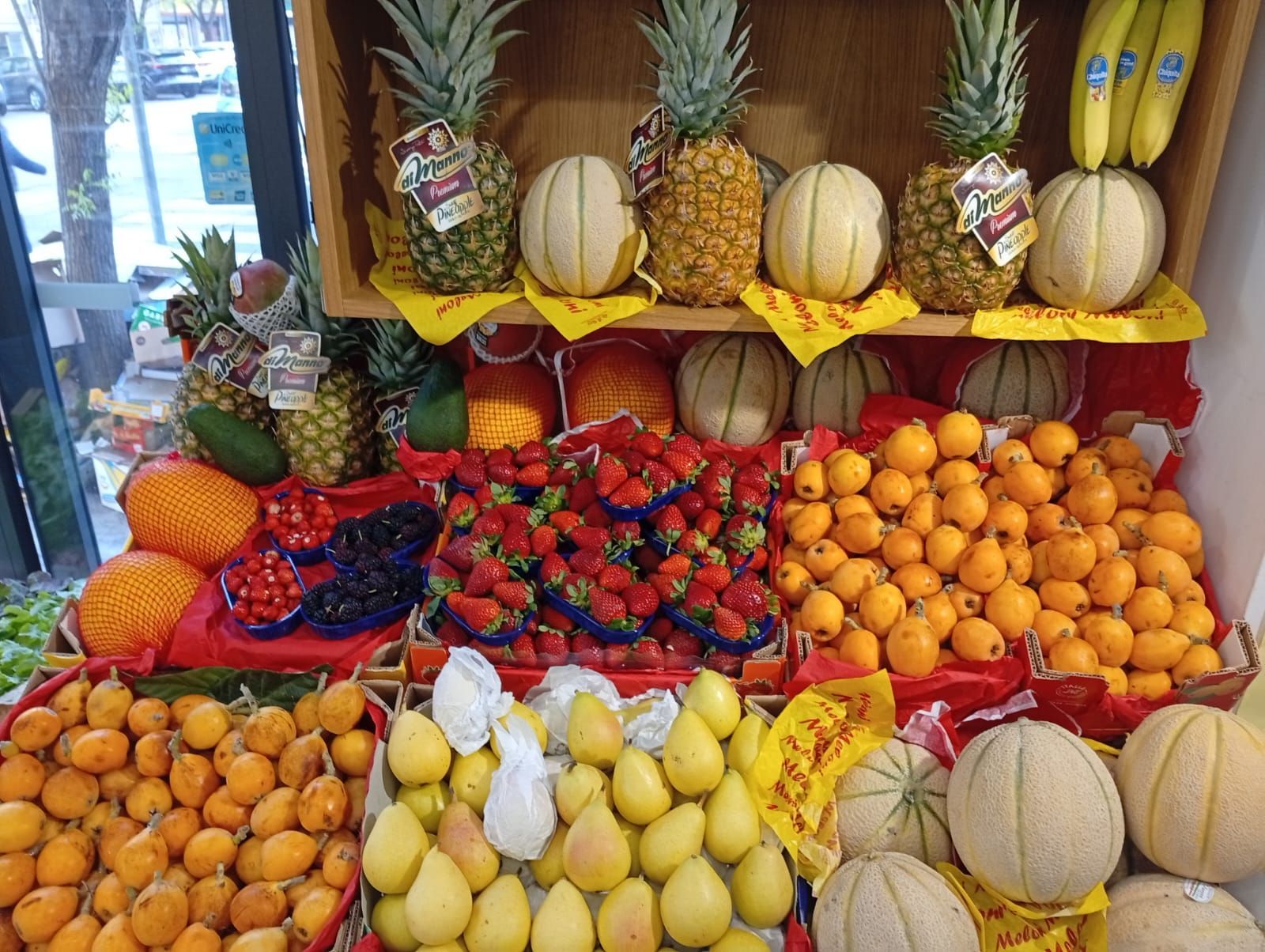 Esposizione di frutta: ananas, meloni cantalupo, arance, bacche, pere e albicocche sugli scaffali.