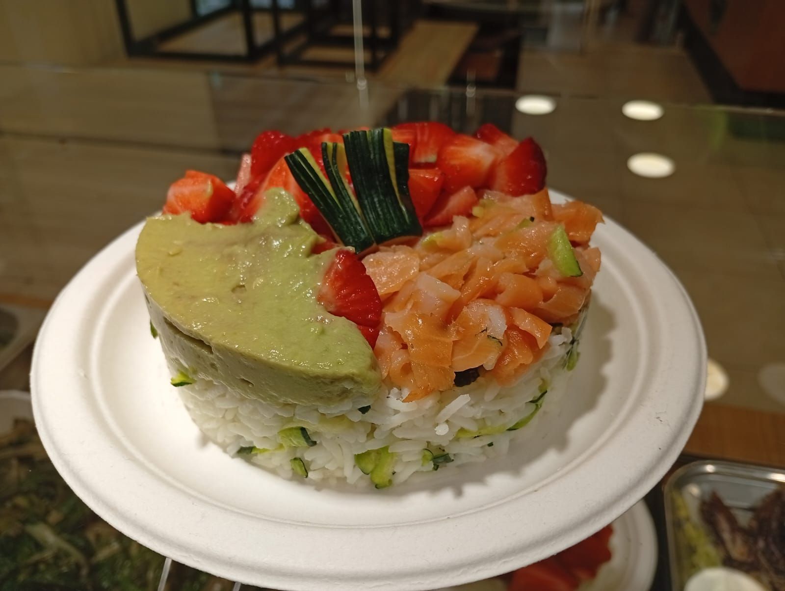 Torta di sushi con avocado, fragole e salmone su un piatto bianco.