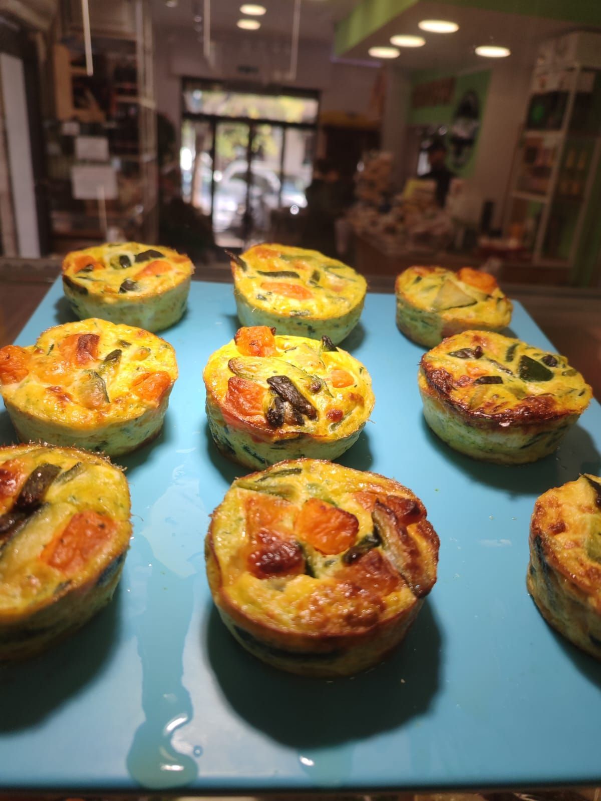 Quiche di verdure cotte al forno su un vassoio blu, in una vetrina da forno ben illuminata.