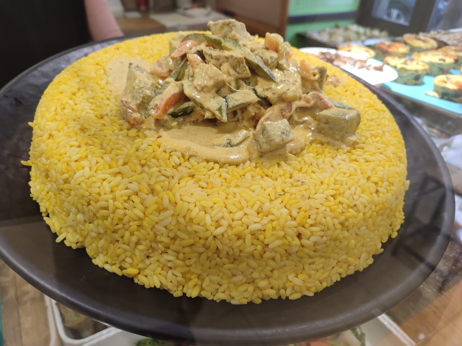 Cupola di riso giallo condita con curry cremoso di verdure su un piatto nero.