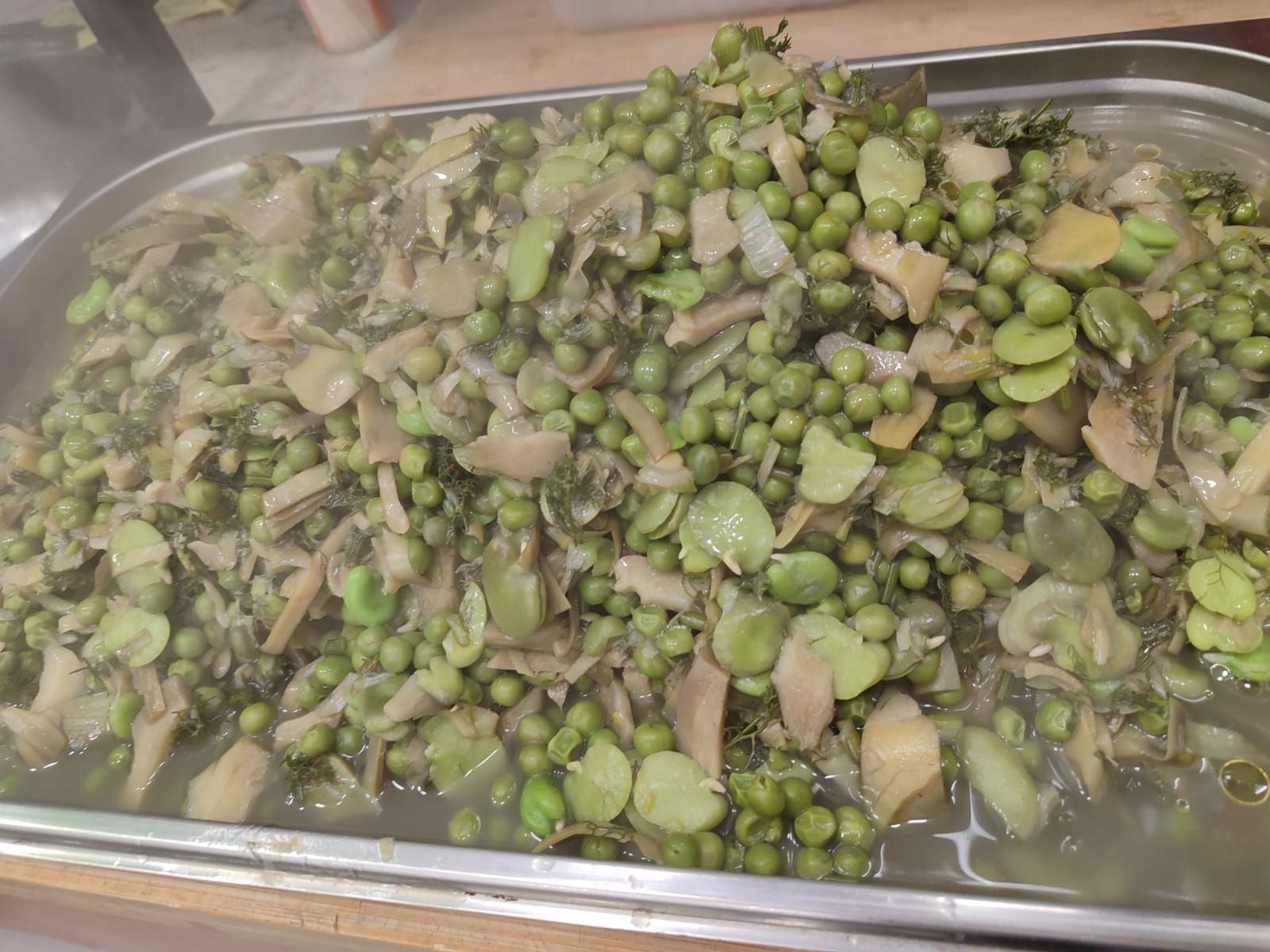 Vassoio fumante di verdure miste: piselli, fave e cuori di carciofo.