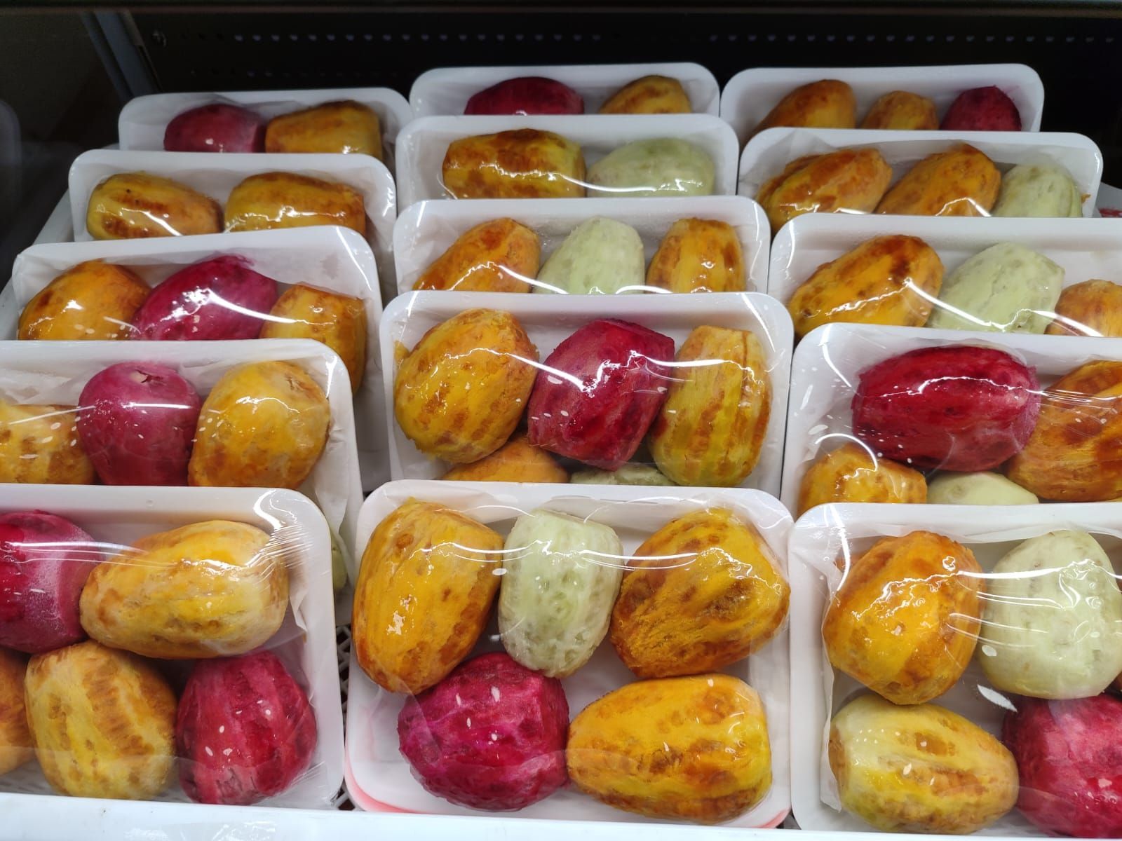 Frutta preconfezionata esposta in un negozio, di vari colori: rosa, giallo e verde.