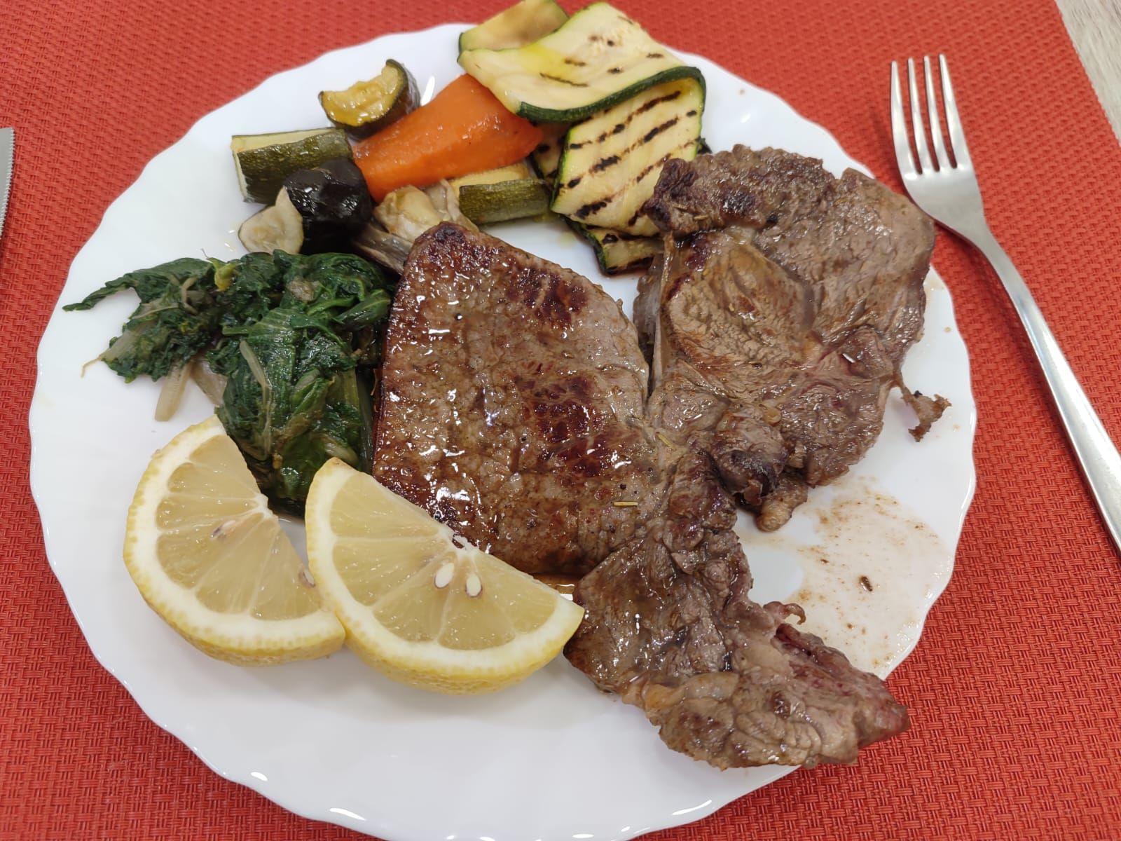 Piatto di bistecca alla griglia, verdure e fette di limone.