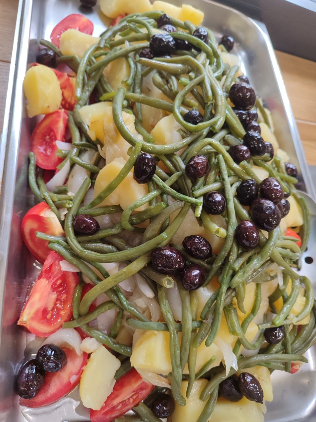 Insalata di patate con fagiolini, olive, pomodori e cipolla su un piatto d'argento.
