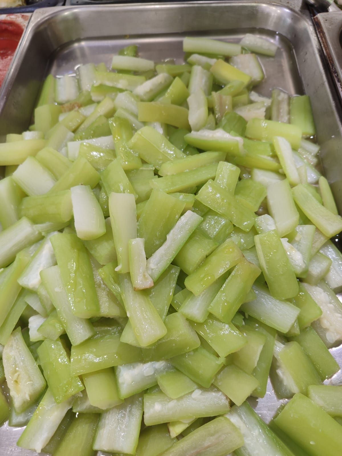Verdure verdi tritate in un vassoio di metallo, probabilmente in un buffet o in un locale di ristorazione.