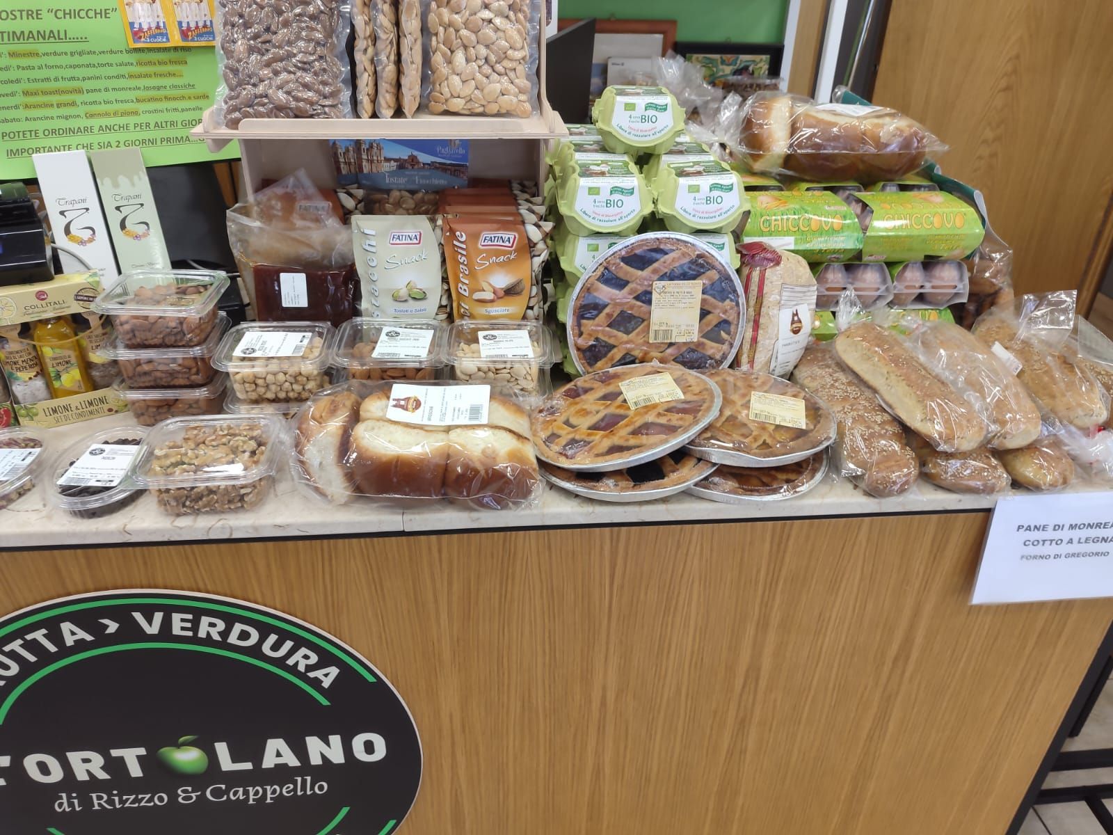 Esposizione di prodotti da forno e alimenti confezionati in un negozio, tra cui torte, pane e frutta secca.