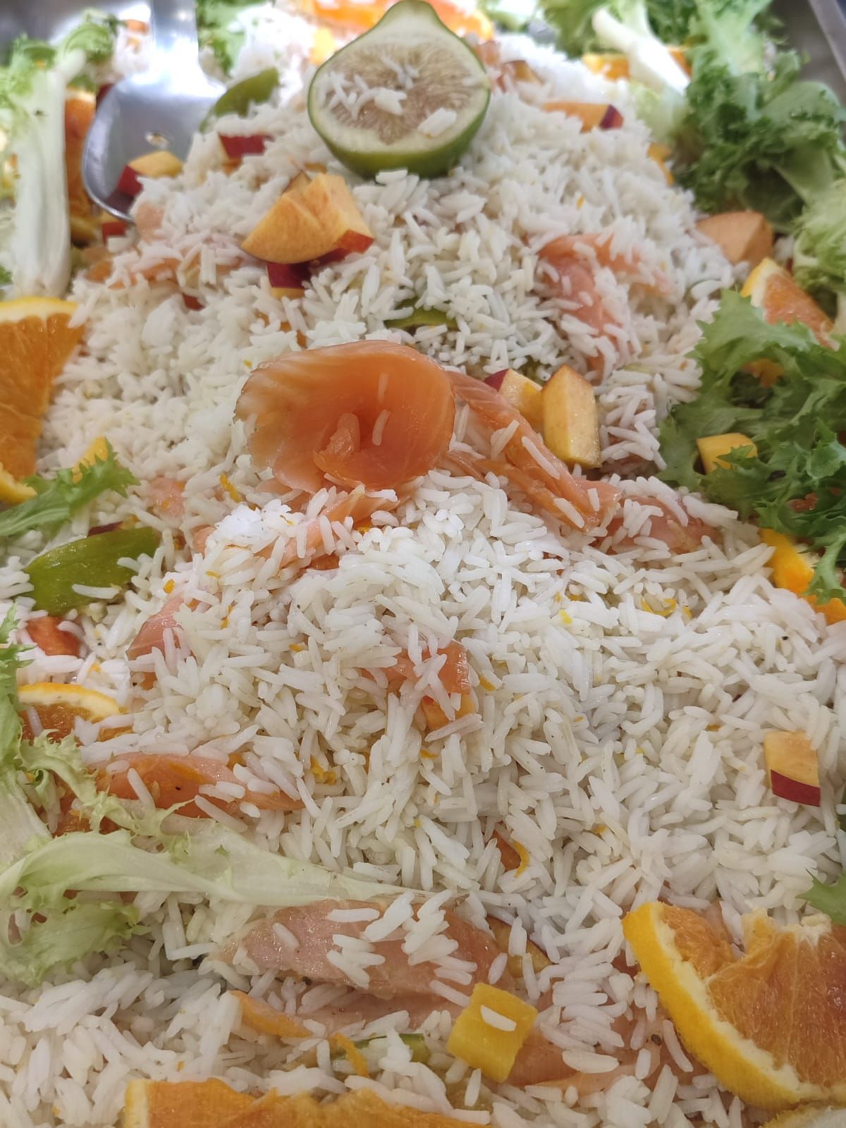 Insalata di riso con fette d'arancia, peperoni verdi e contorno di lattuga.