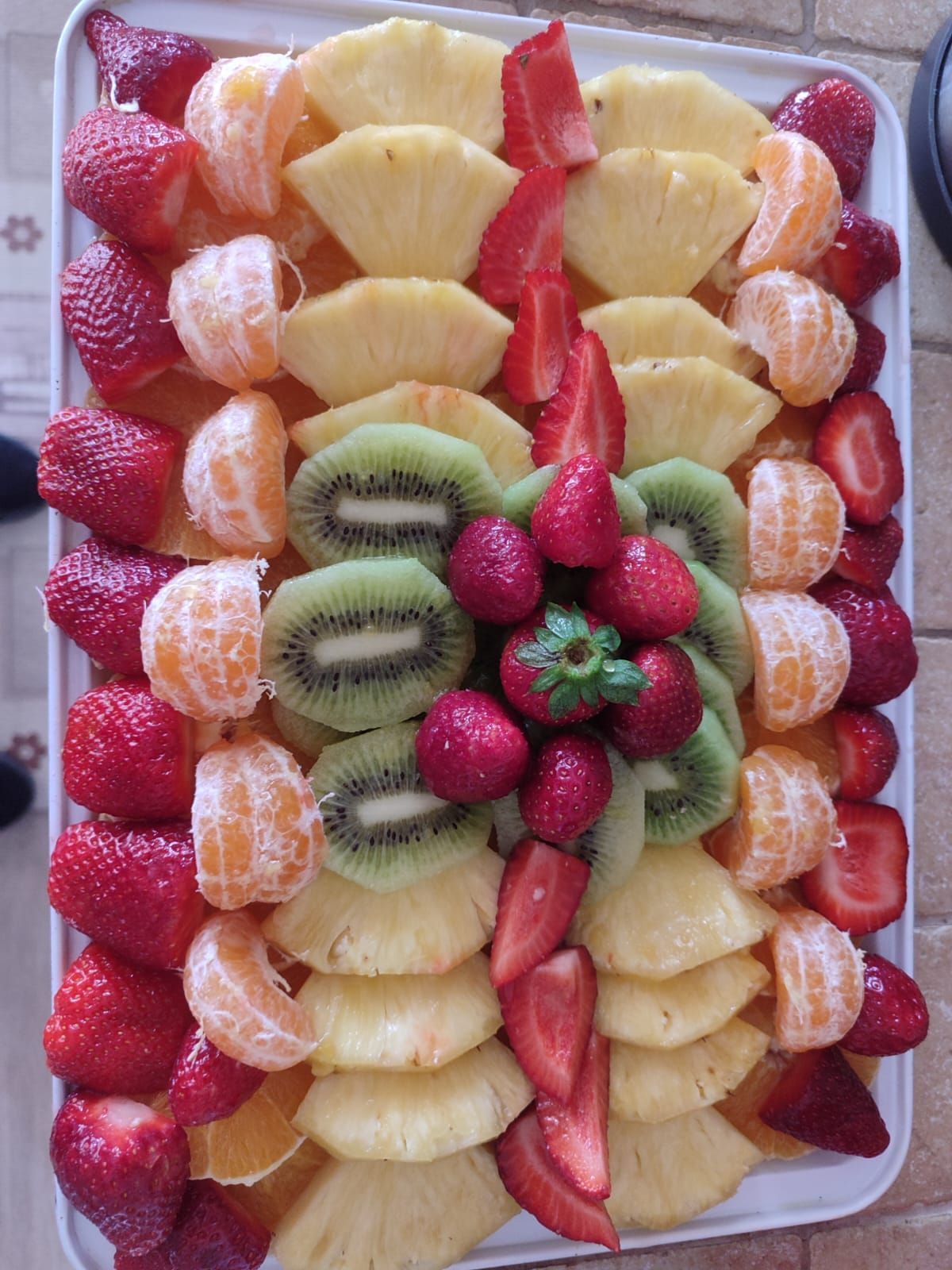 Piatto di frutta con fragole, ananas, kiwi e mandarini, disposti su un vassoio bianco.