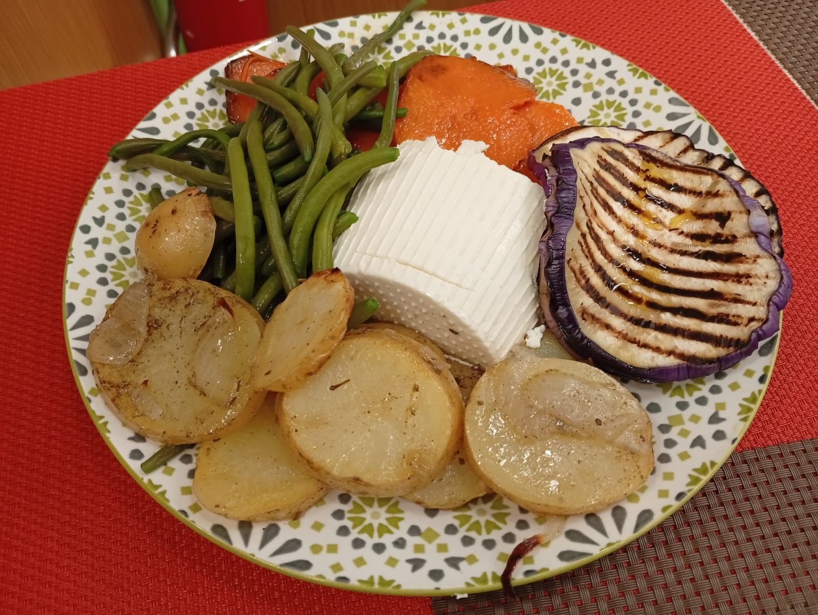 Piatto di verdure arrostite, tra cui fagiolini, patate, zucca e melanzane grigliate, con un blocco di formaggio bianco.