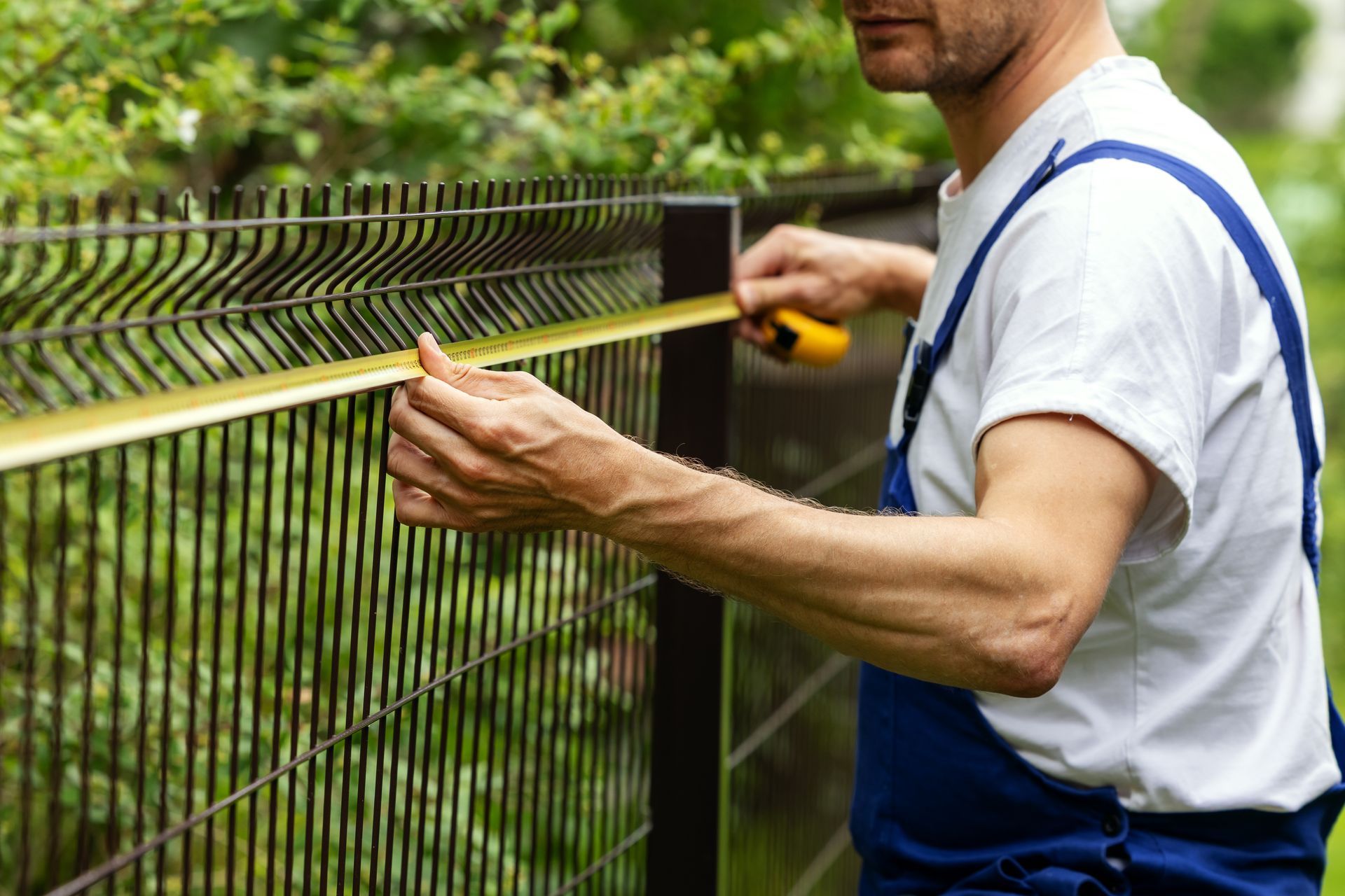 Worker taking measurements with measuring tape for new fence.