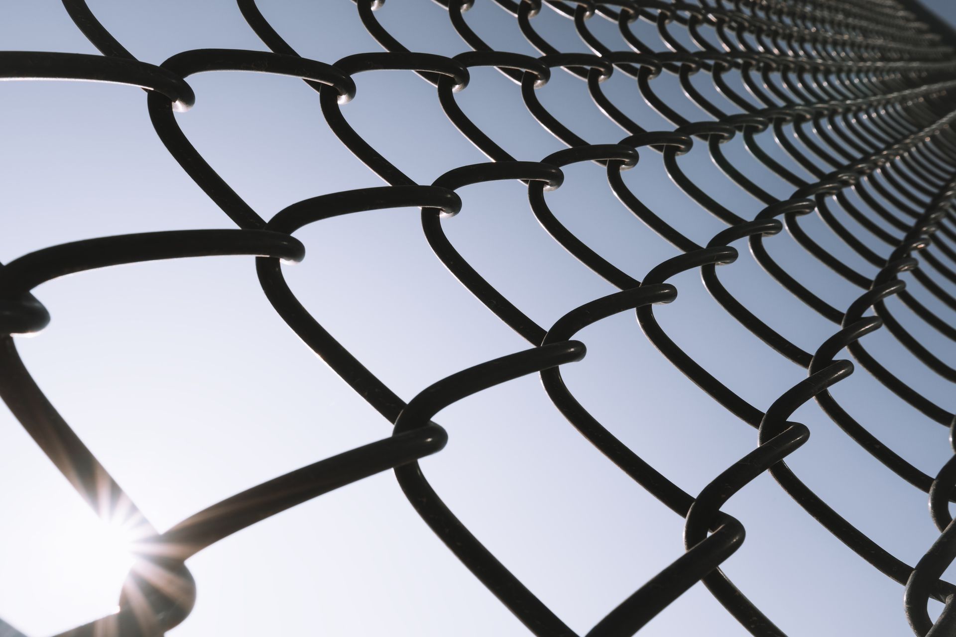 Looking up at a chain link fence with the sun shining through it