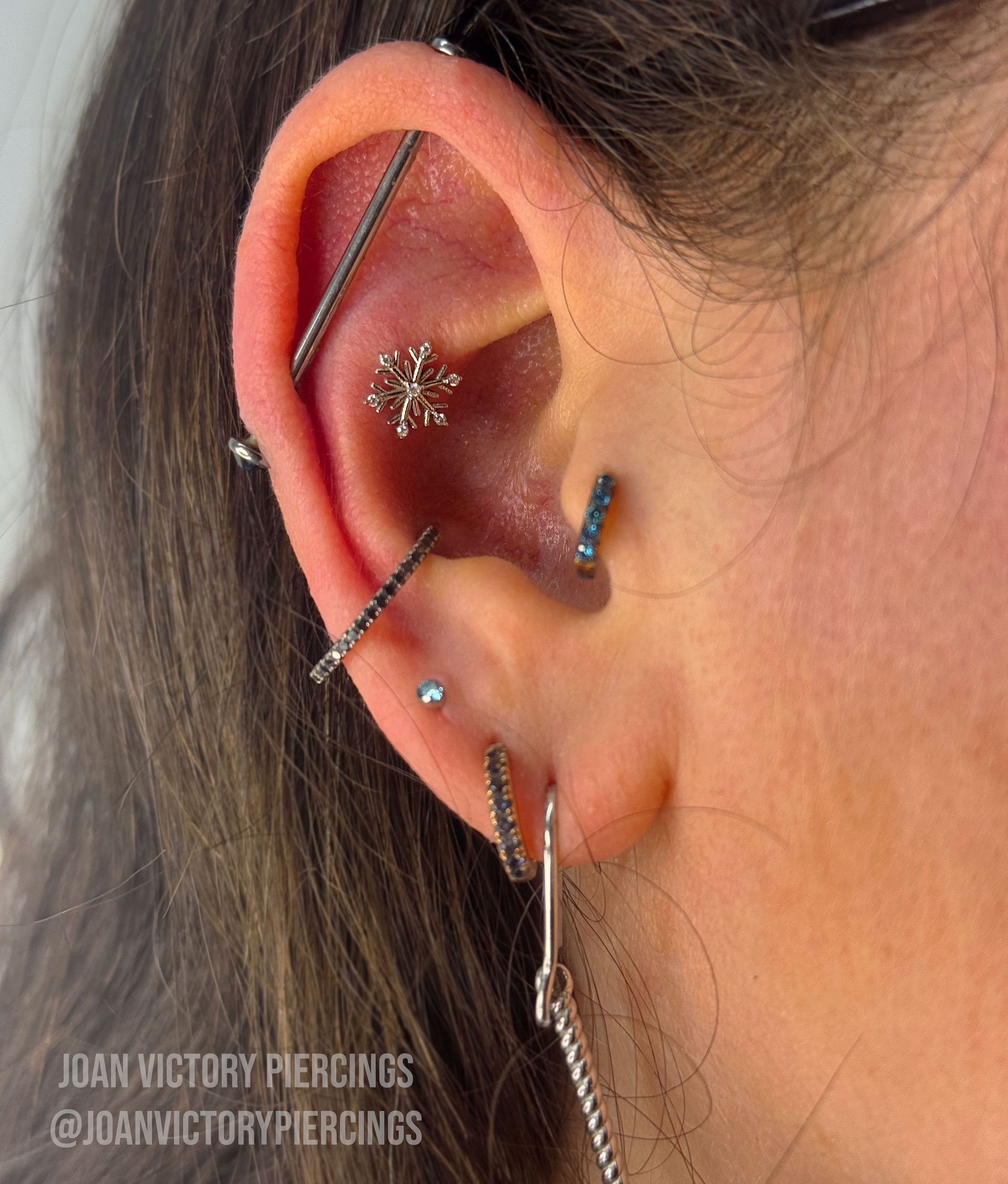 Ear with multiple piercings, including an industrial, snowflake stud, and dangling earrings.